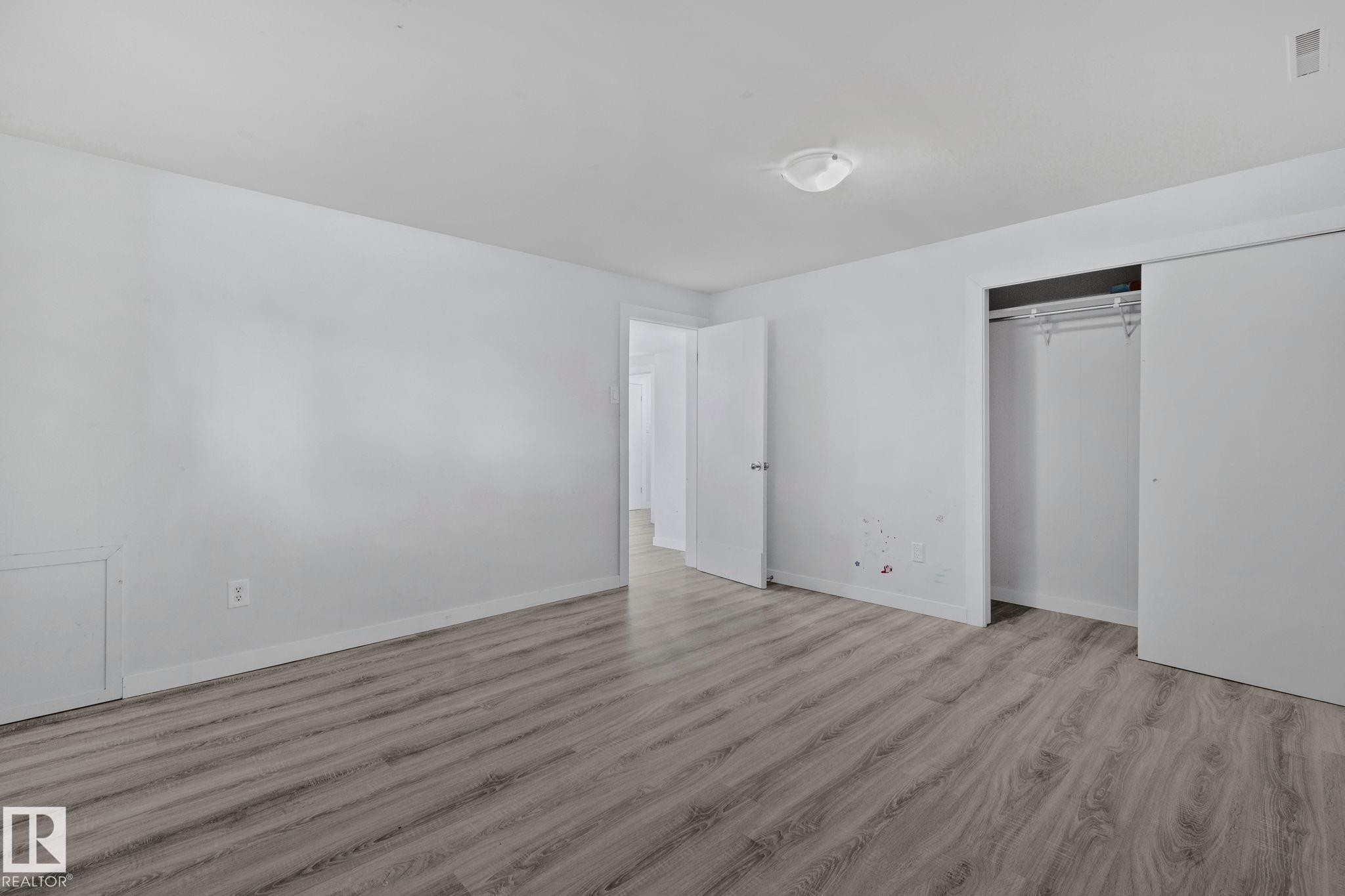 This room features light-colored walls, wood-style flooring, a ceiling-mounted light fixture, and a closet with sliding doors and a hanging rod - 12002 37 Street, Edmonton, AB - Indoor Photo Showing Other Room