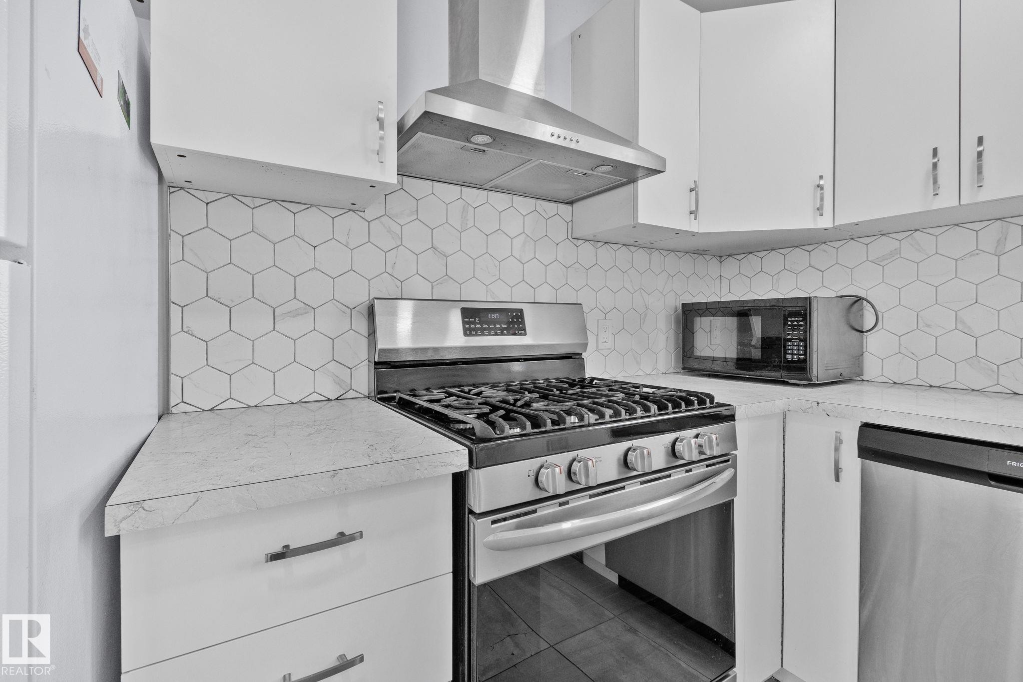 The kitchen features white cabinetry, a hexagonal tiled backsplash, a stainless steel range with a matching range hood, and a built-in dishwasher - 12002 37 Street, Edmonton, AB - Indoor Photo Showing Kitchen