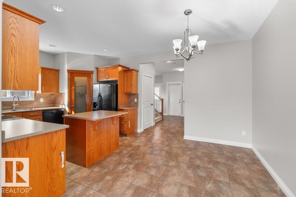 Kitchen with wood cabinetry, a center island, dark appliances, and a pantry with a frosted glass door - 16419 53 Street, Edmonton, AB - Indoor Photo Showing Kitchen