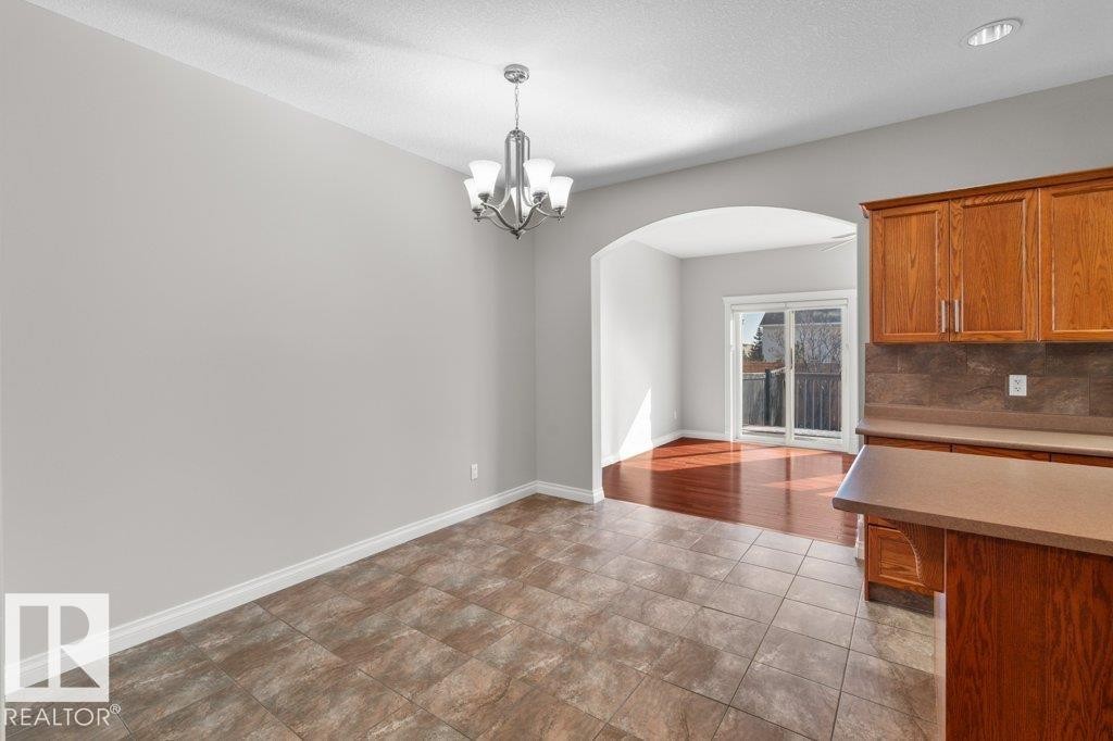 This property features an open layout with tiled flooring, a contemporary chandelier, and an archway leading to a room with hardwood flooring and sliding glass doors - 16419 53 Street, Edmonton, AB - Indoor