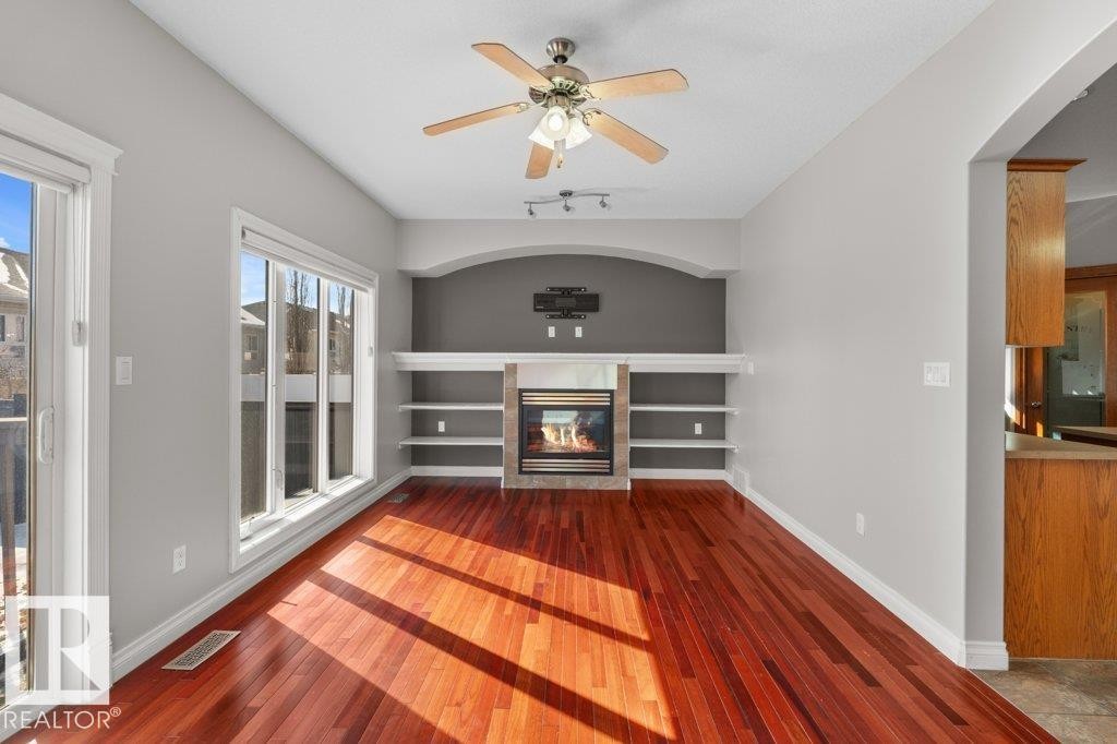 Living area featuring hardwood floors, large windows, a ceiling fan, and a fireplace with built-in shelving - 16419 53 Street, Edmonton, AB - Indoor Photo Showing Other Room With Fireplace