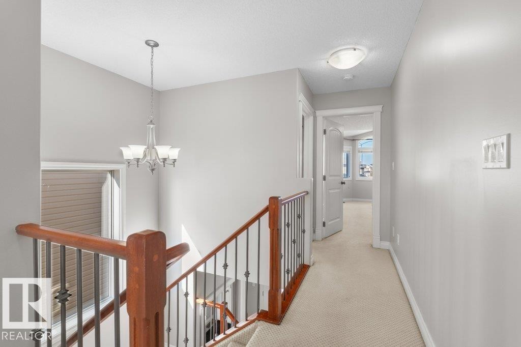 The property features a staircase with a wooden banister and wrought iron spindles, leading to a carpeted hallway - 16419 53 Street, Edmonton, AB - Indoor Photo Showing Other Room