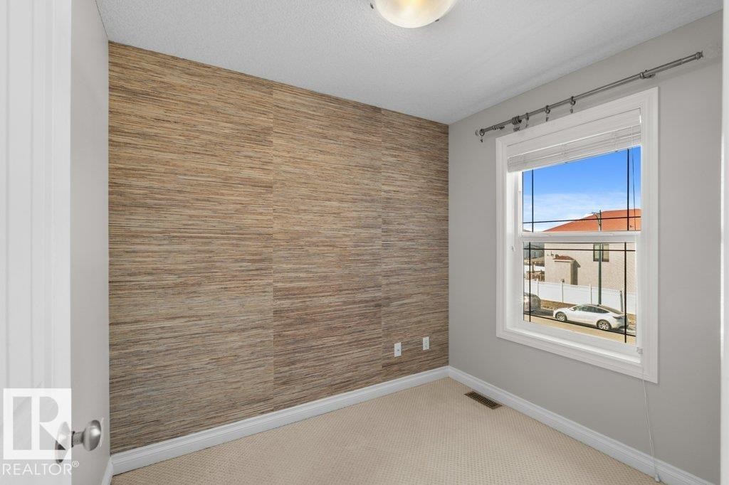 This room features a textured accent wall, light-colored carpeting, and a window with blinds providing natural light - 16419 53 Street, Edmonton, AB - Indoor Photo Showing Other Room