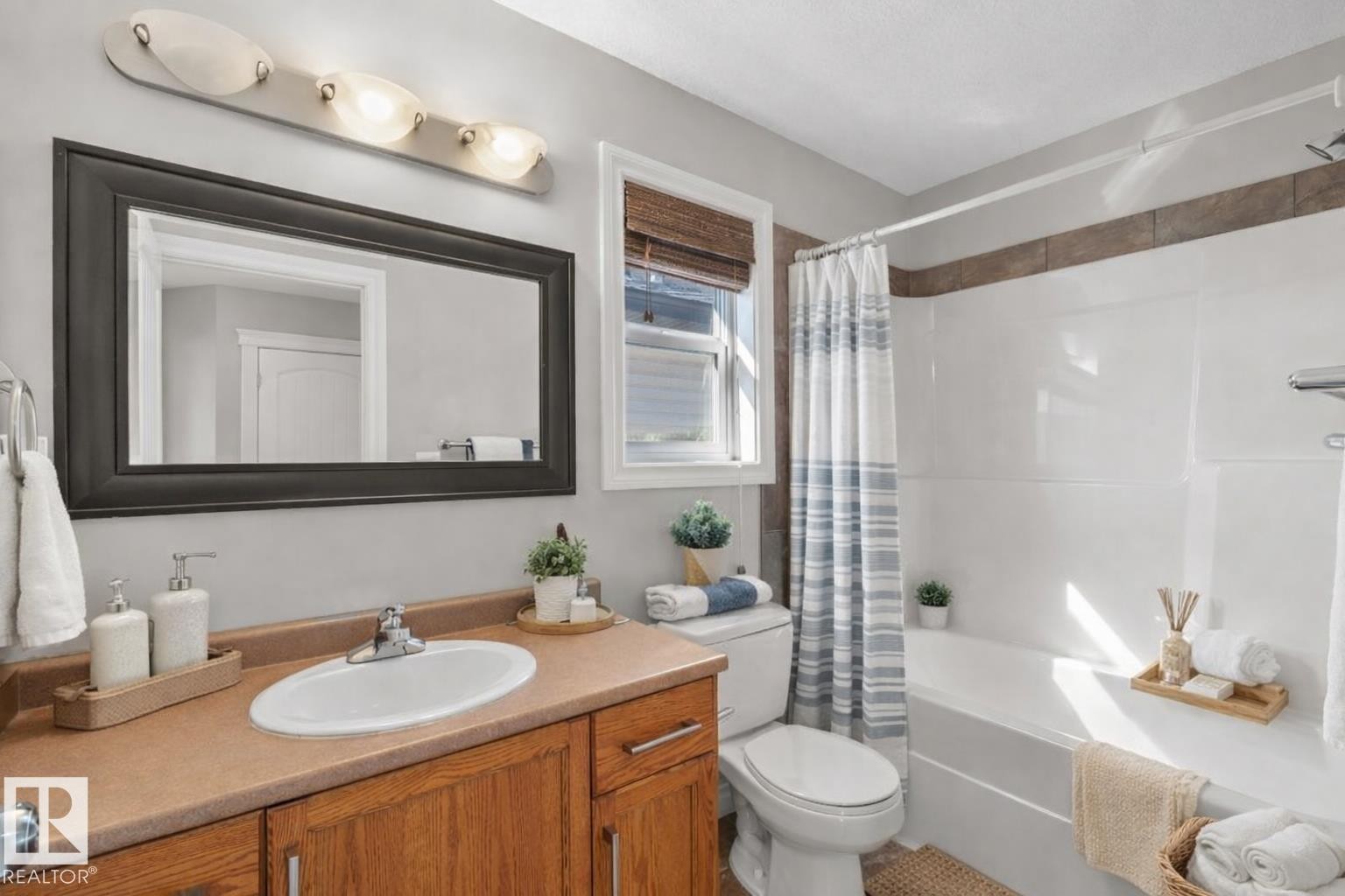 The bathroom features a vanity with a countertop and an integrated sink, a framed mirror, and a window with blinds - 16419 53 Street, Edmonton, AB - Indoor Photo Showing Bathroom