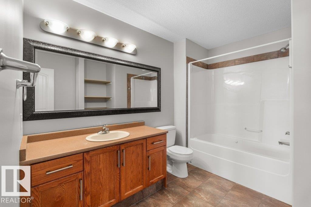 This bathroom features a spacious vanity with wood cabinetry, a large mirror with a dark frame, and a combination bathtub and shower with tiled accents - 16419 53 Street, Edmonton, AB - Indoor Photo Showing Bathroom