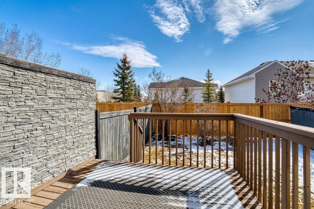 The property features an outdoor deck area with a wood railing and a textured stone wall - 16419 53 Street, Edmonton, AB - Outdoor With Deck Patio Veranda
