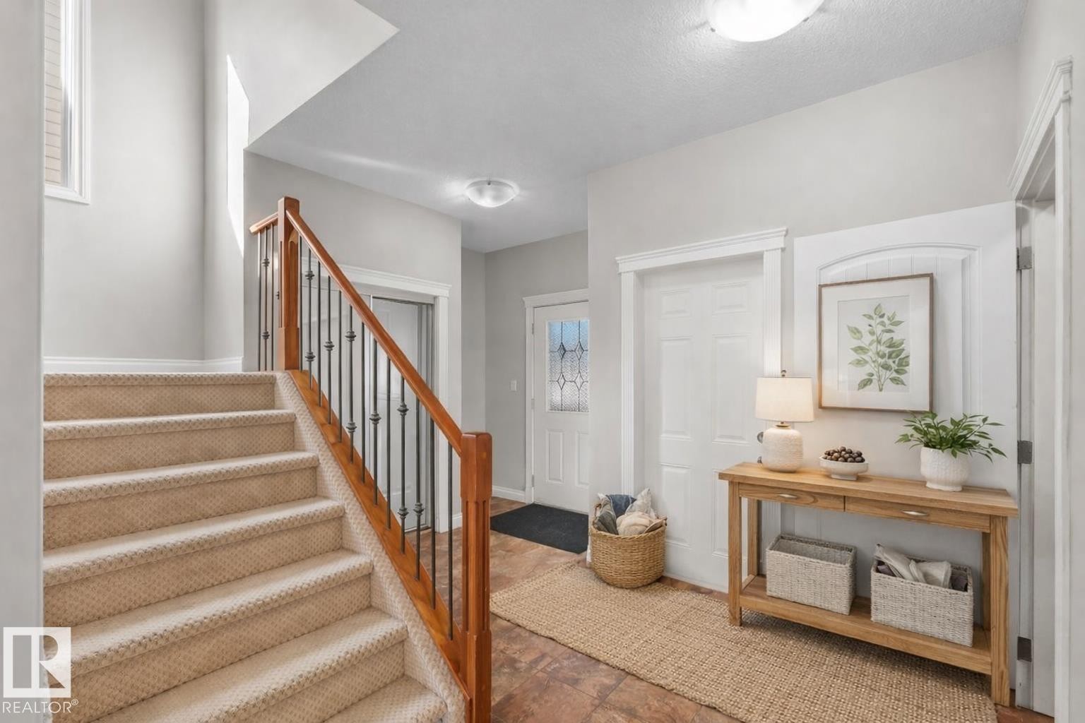 Entryway featuring a carpeted staircase with a wood and wrought iron railing, a front door with decorative glass, and a tiled floor - 16419 53 Street, Edmonton, AB - Indoor Photo Showing Other Room