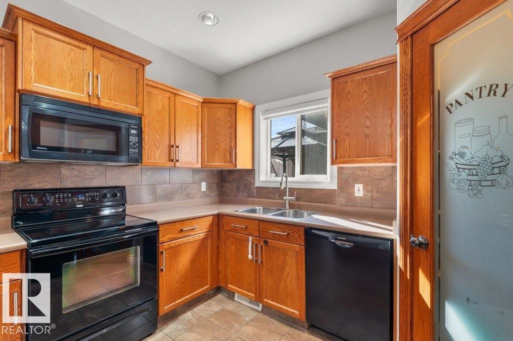 The kitchen features wood cabinetry, a built-in microwave, an electric range, and a dishwasher - 16419 53 Street, Edmonton, AB - Indoor Photo Showing Kitchen With Double Sink