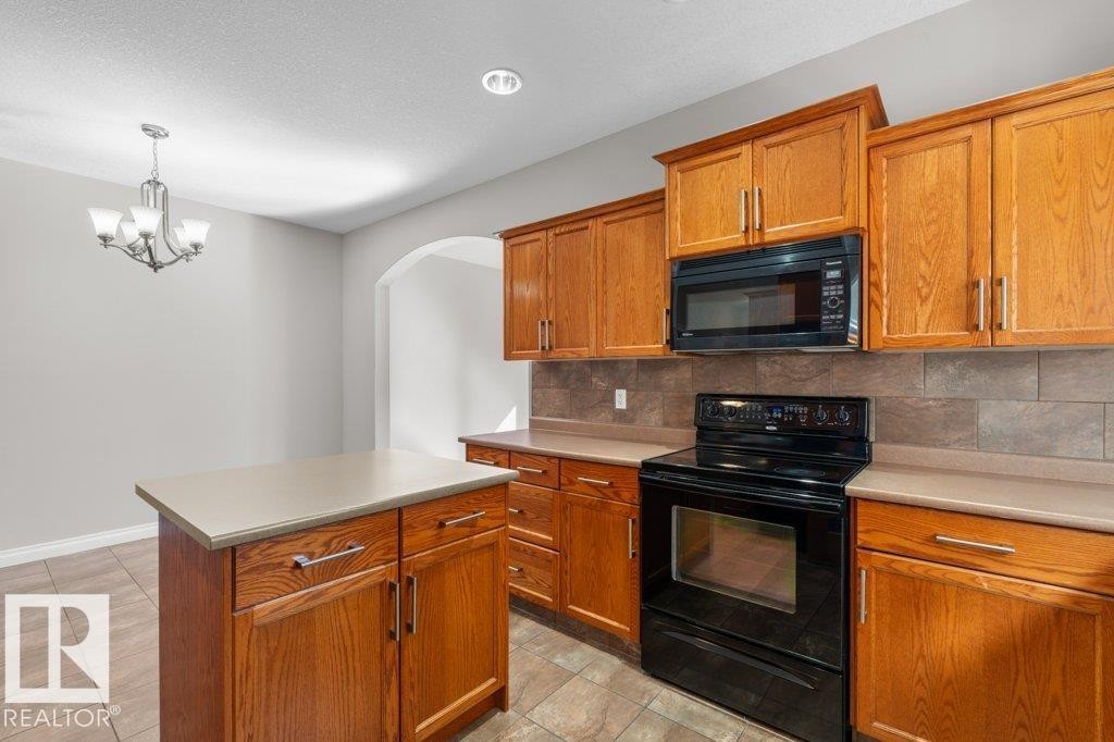 The kitchen features wood cabinetry, black appliances, and a tiled backsplash - 16419 53 Street, Edmonton, AB - Indoor Photo Showing Kitchen