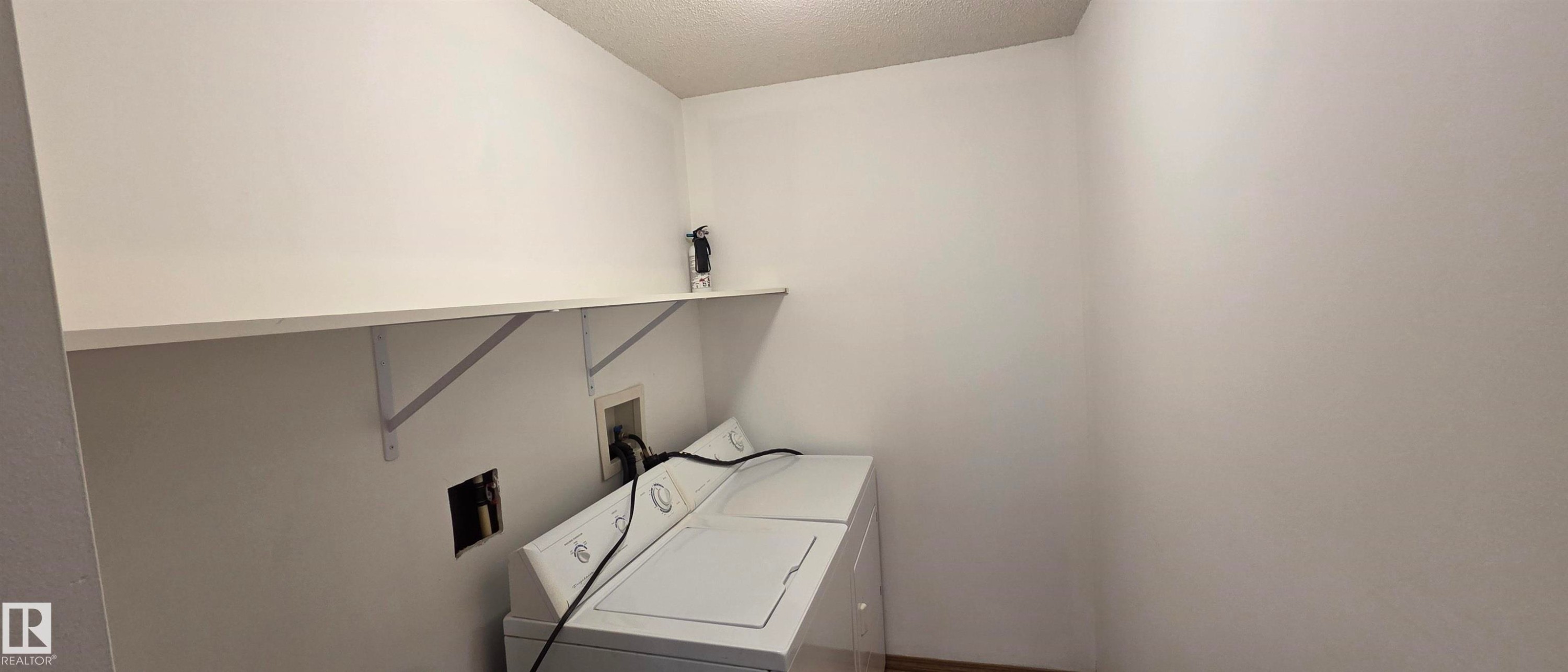 This utility space features a white shelf, a white washing machine, and a white dryer - 208A 260 Spruce Ridge Road, Spruce Grove, AB - Indoor