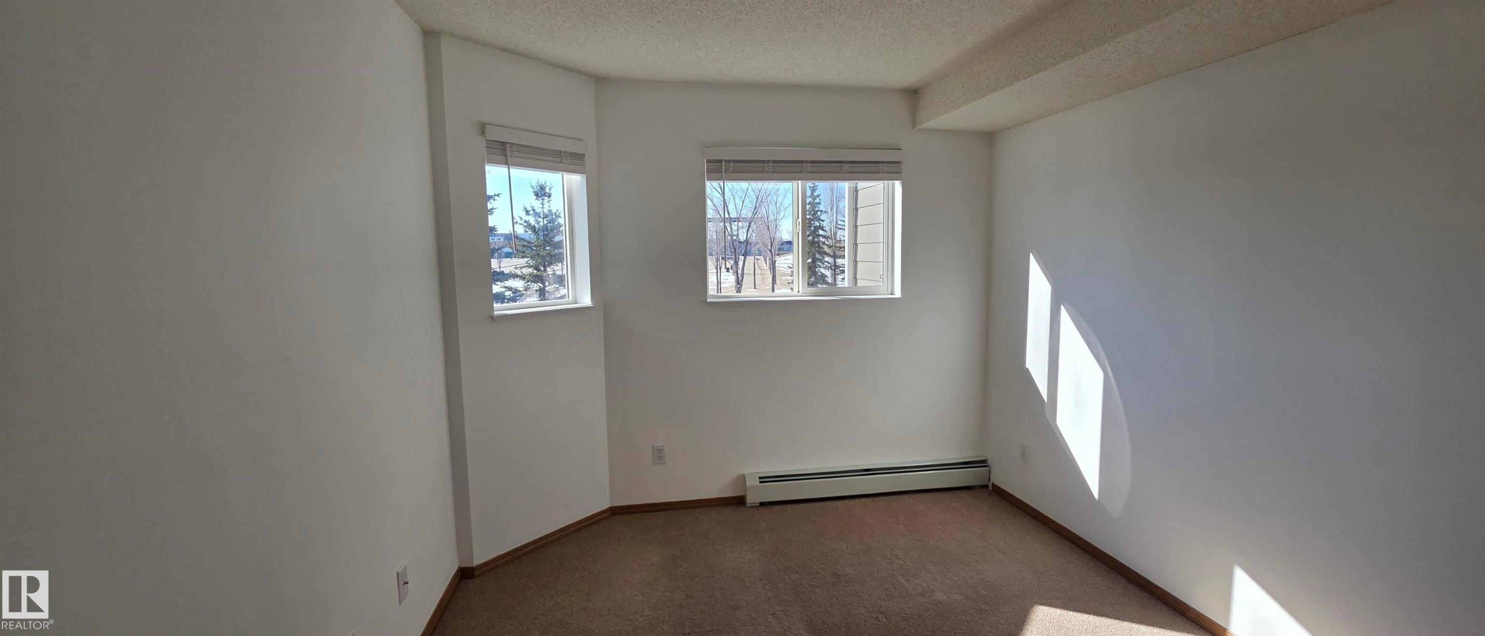 This space features two windows with blinds, providing natural light, and a baseboard heater - 208A 260 Spruce Ridge Road, Spruce Grove, AB - Indoor Photo Showing Other Room