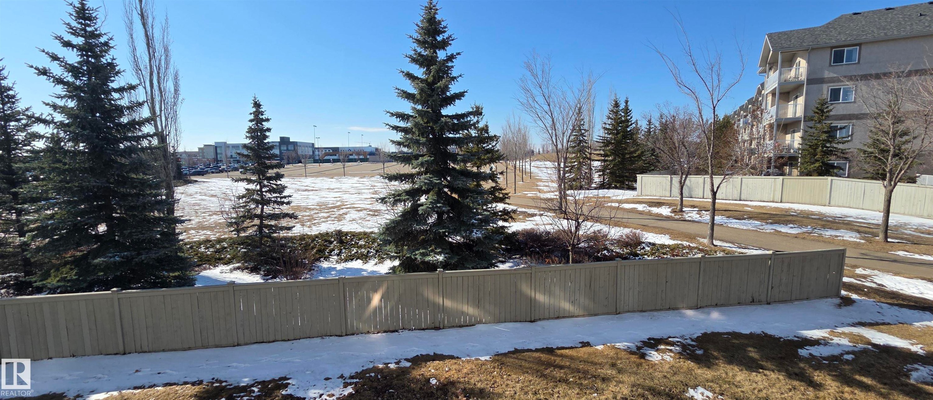 Surrounding landscape featuring evergreen trees, a wooden fence, and a paved pathway - 208A 260 Spruce Ridge Road, Spruce Grove, AB - Outdoor