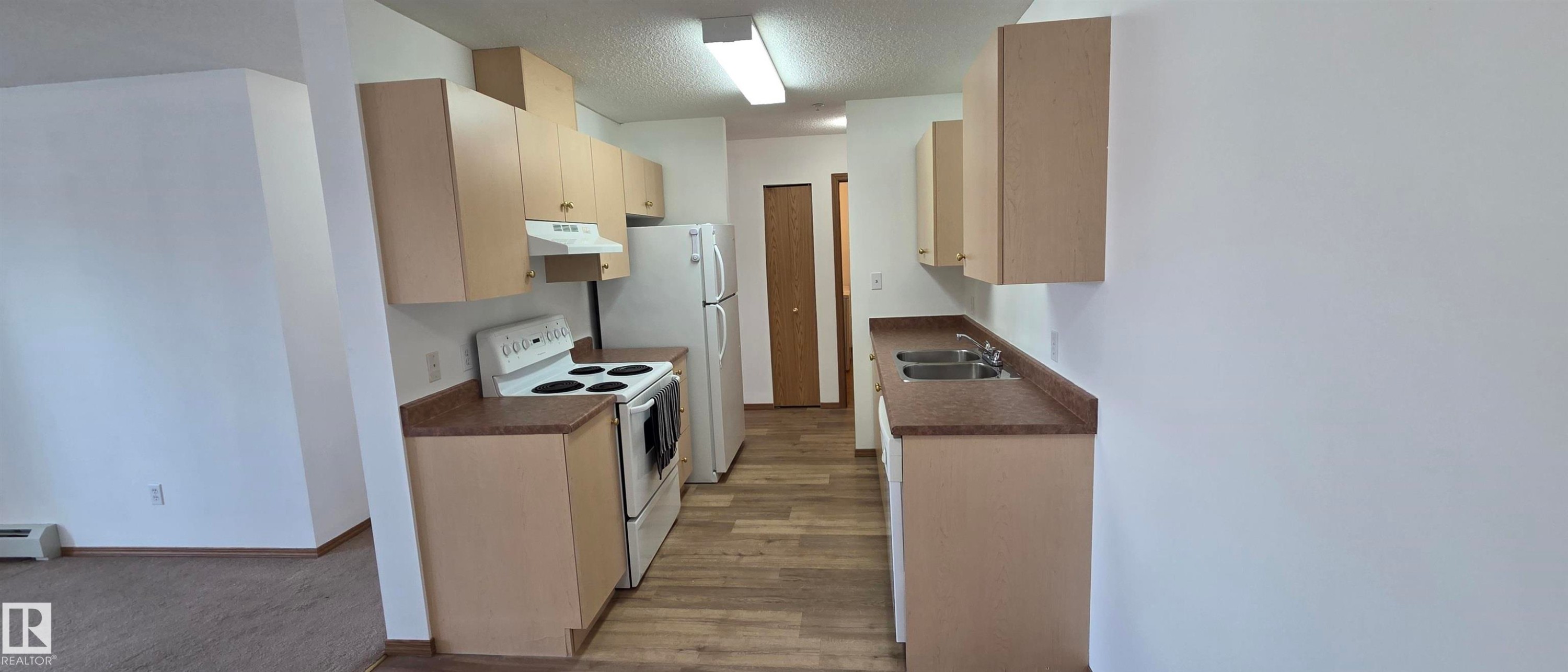 Well-maintained kitchen featuring light-colored cabinetry, laminate countertops, and essential appliances including a refrigerator, stove, and double sink - 208A 260 Spruce Ridge Road, Spruce Grove, AB - Indoor Photo Showing Kitchen With Double Sink