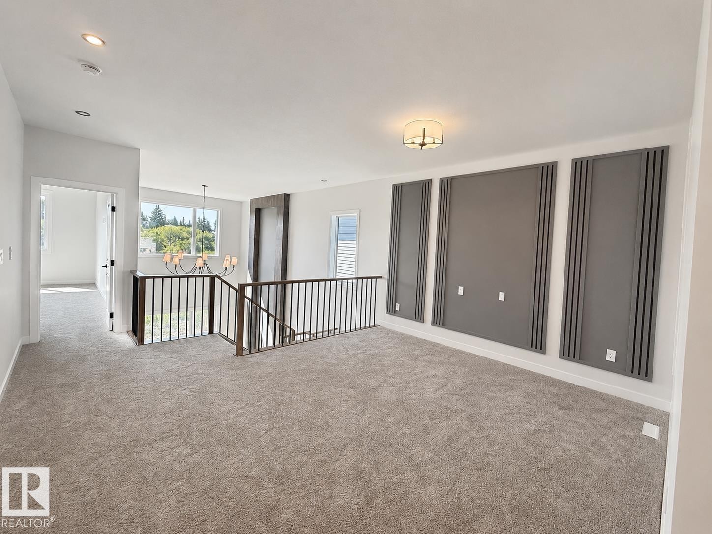 Expansive carpeted area featuring a prominent staircase with dark metal railings, a contemporary chandelier, recessed lighting, and decorative wall panels - 22 Meadowgrove Landing, Spruce Grove, AB - Indoor Photo Showing Other Room