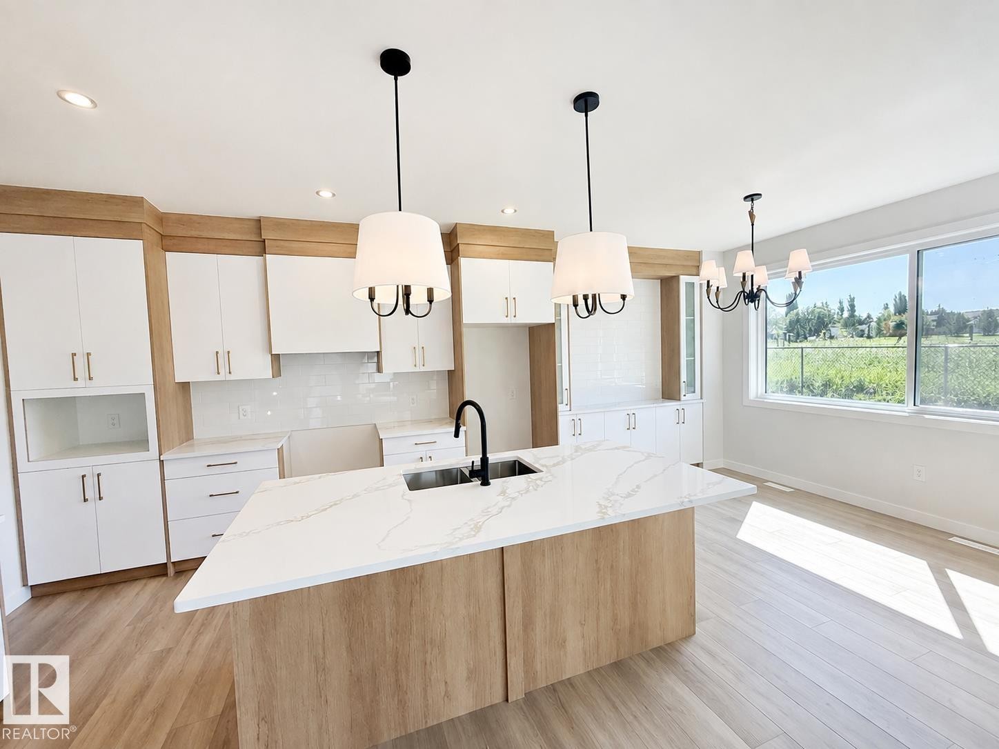 Expansive kitchen featuring a large central island, white cabinetry with wood-finish accents, quartz countertops, and integrated stainless steel sink with a matte black faucet - 22 Meadowgrove Landing, Spruce Grove, AB - Indoor Photo Showing Kitchen