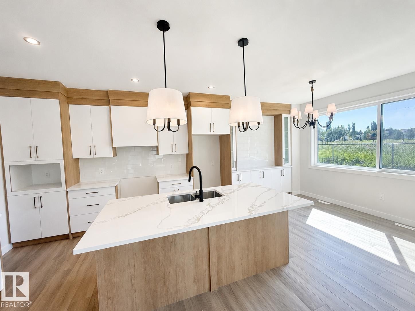 Kitchen featuring a large island with a waterfall-edge countertop, two-tone cabinetry, white tile backsplash, and contemporary pendant lighting - 22 Meadowgrove Landing, Spruce Grove, AB - Indoor Photo Showing Kitchen