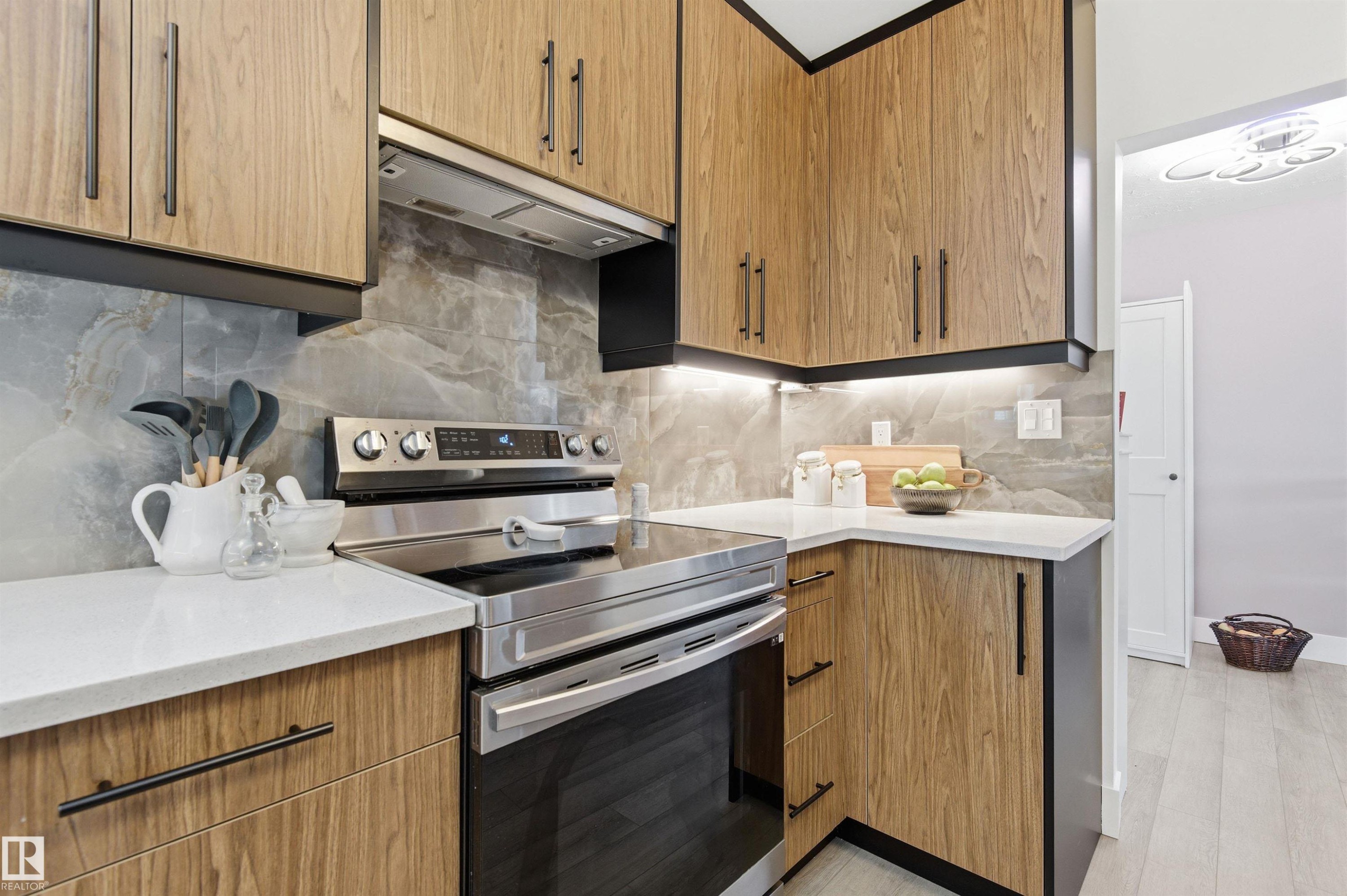 The kitchen features wood cabinetry with black hardware, stainless steel appliances, a grey tiled backsplash, and white countertops - 12904 95 Street, Edmonton, AB - Indoor Photo Showing Kitchen