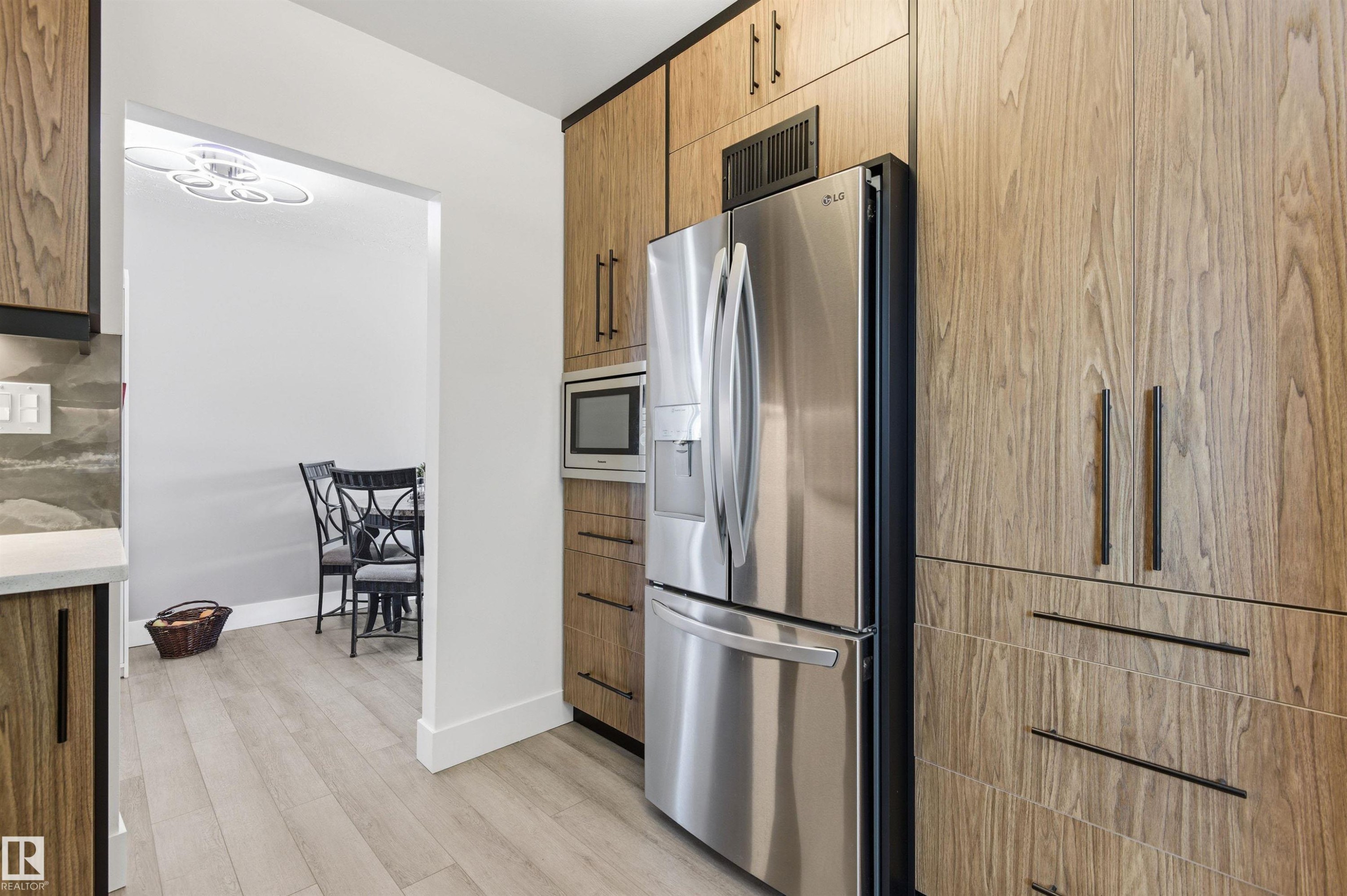 Kitchen featuring wood-grain cabinetry with dark hardware, a stainless steel refrigerator, and a built-in microwave - 12904 95 Street, Edmonton, AB - Indoor Photo Showing Kitchen