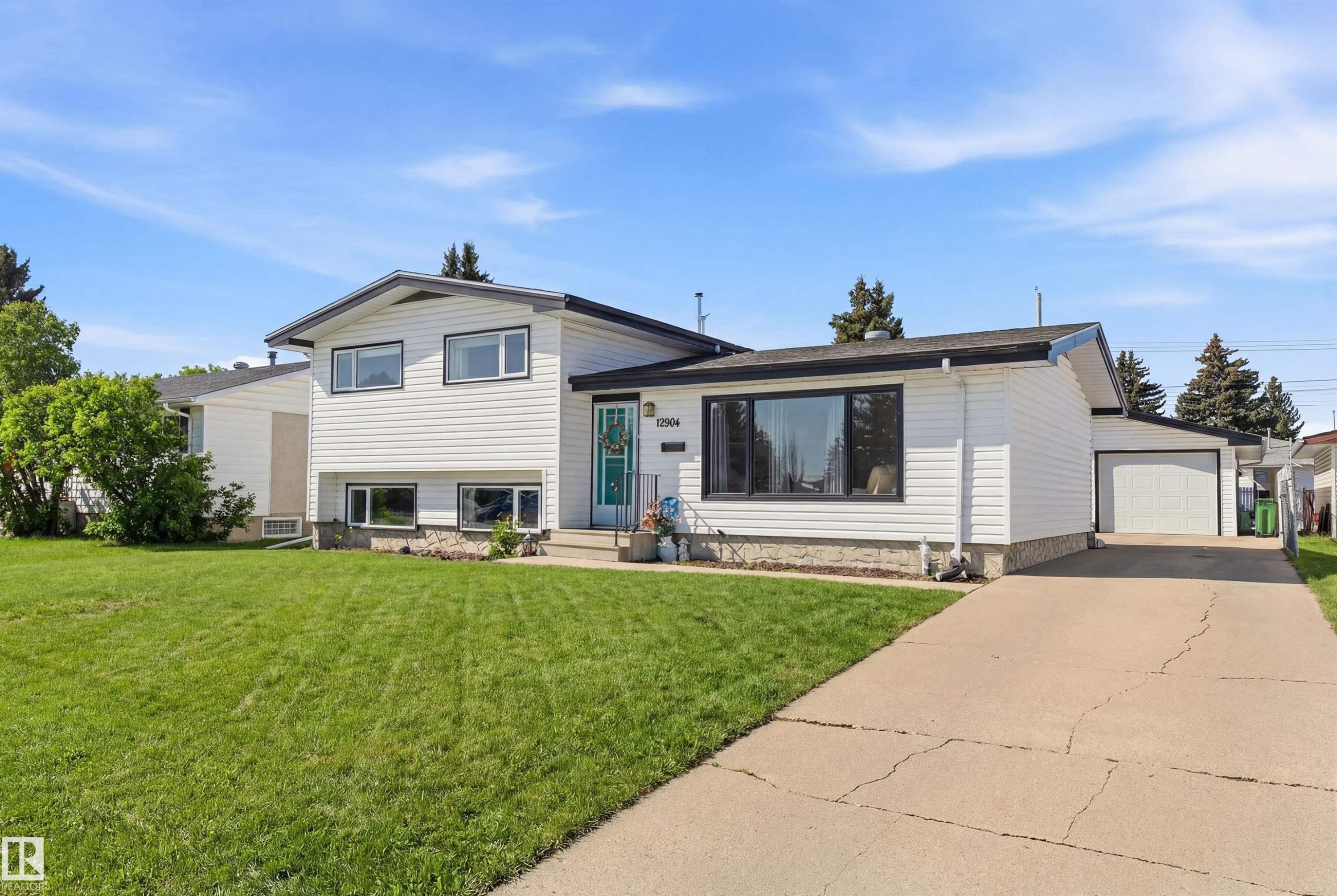 The property features white siding with black trim, a well-maintained lawn, and a paved driveway leading to an attached garage - 12904 95 Street, Edmonton, AB - Outdoor