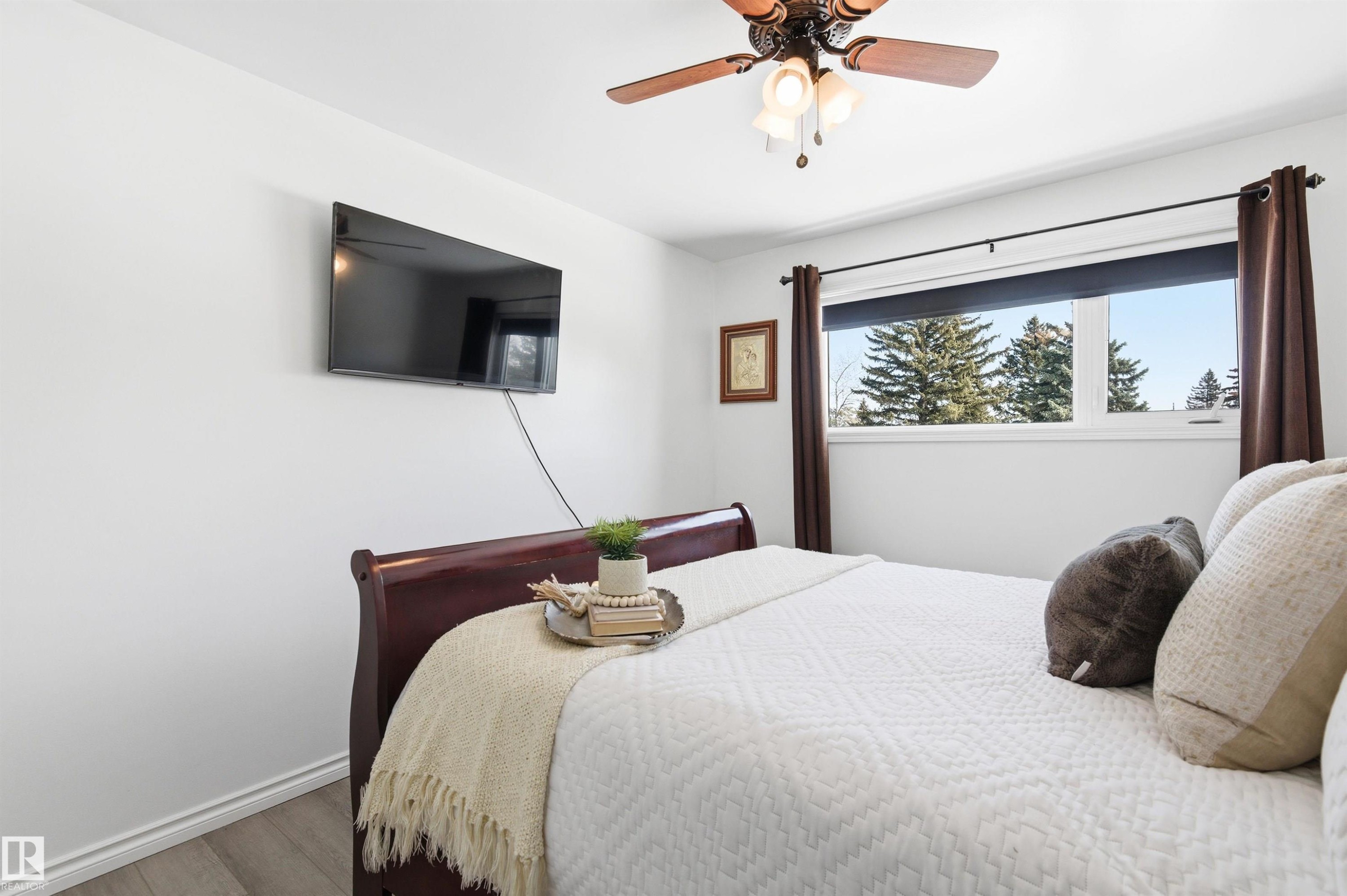 This room features a ceiling fan with integrated lighting, a window with a view of trees, and hard surface flooring - 12904 95 Street, Edmonton, AB - Indoor Photo Showing Bedroom