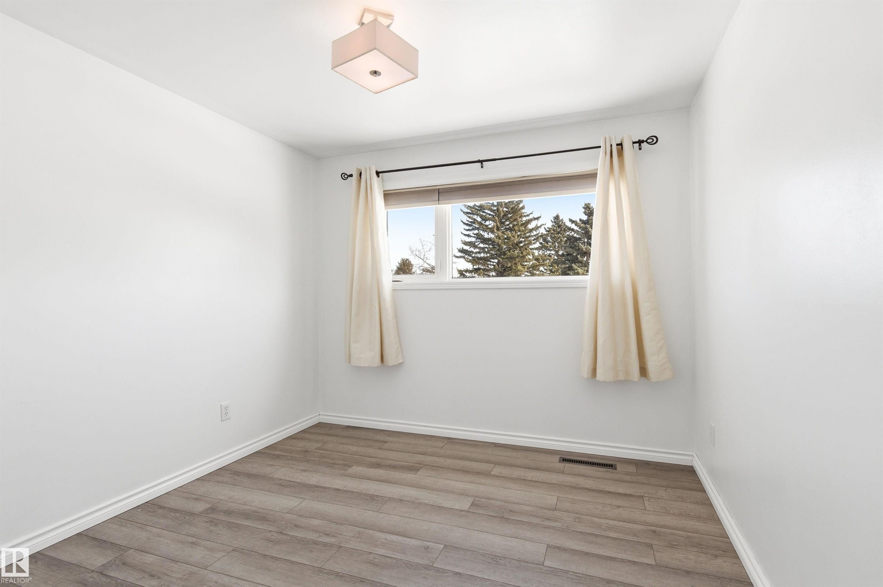 This room features light-colored walls, wood-look flooring, and a window with a view of trees - 12904 95 Street, Edmonton, AB - Indoor Photo Showing Other Room
