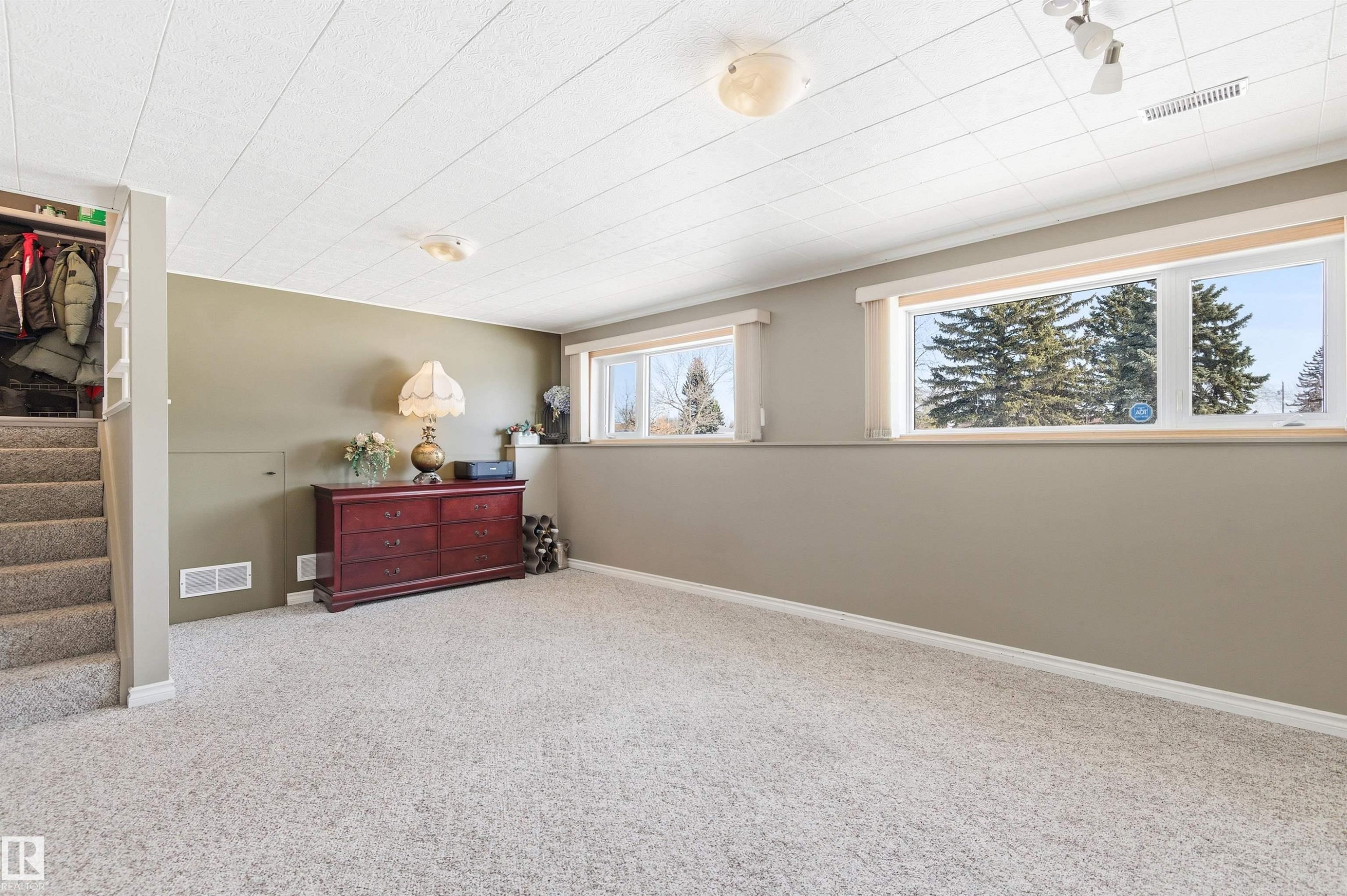This spacious room features light-colored carpeting, multiple windows providing natural light, and a functional staircase - 12904 95 Street, Edmonton, AB - Indoor