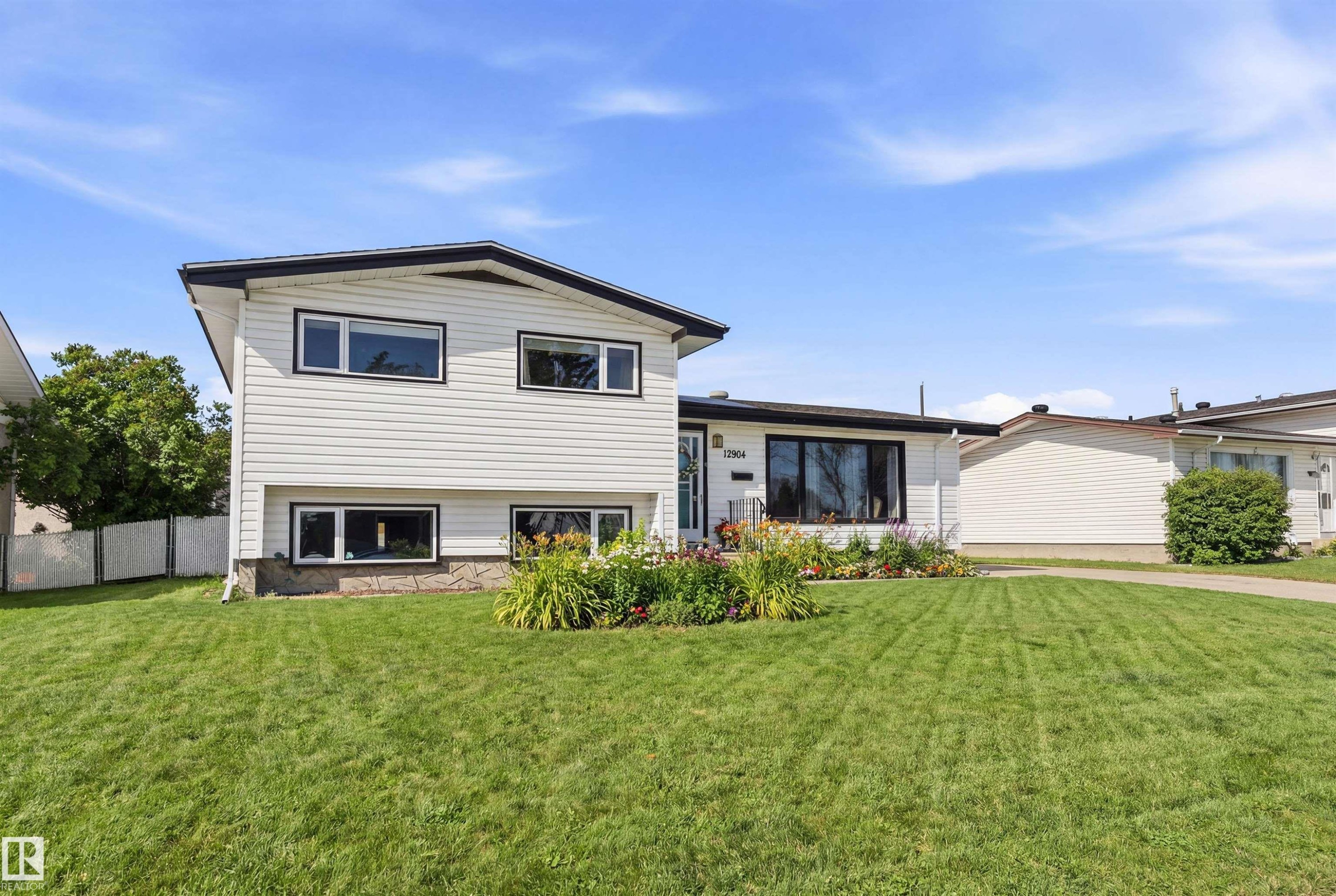 The property features a well-maintained lawn and a flower bed with varied plantings, complementing the white exterior siding and dark trim - 12904 95 Street, Edmonton, AB - Outdoor