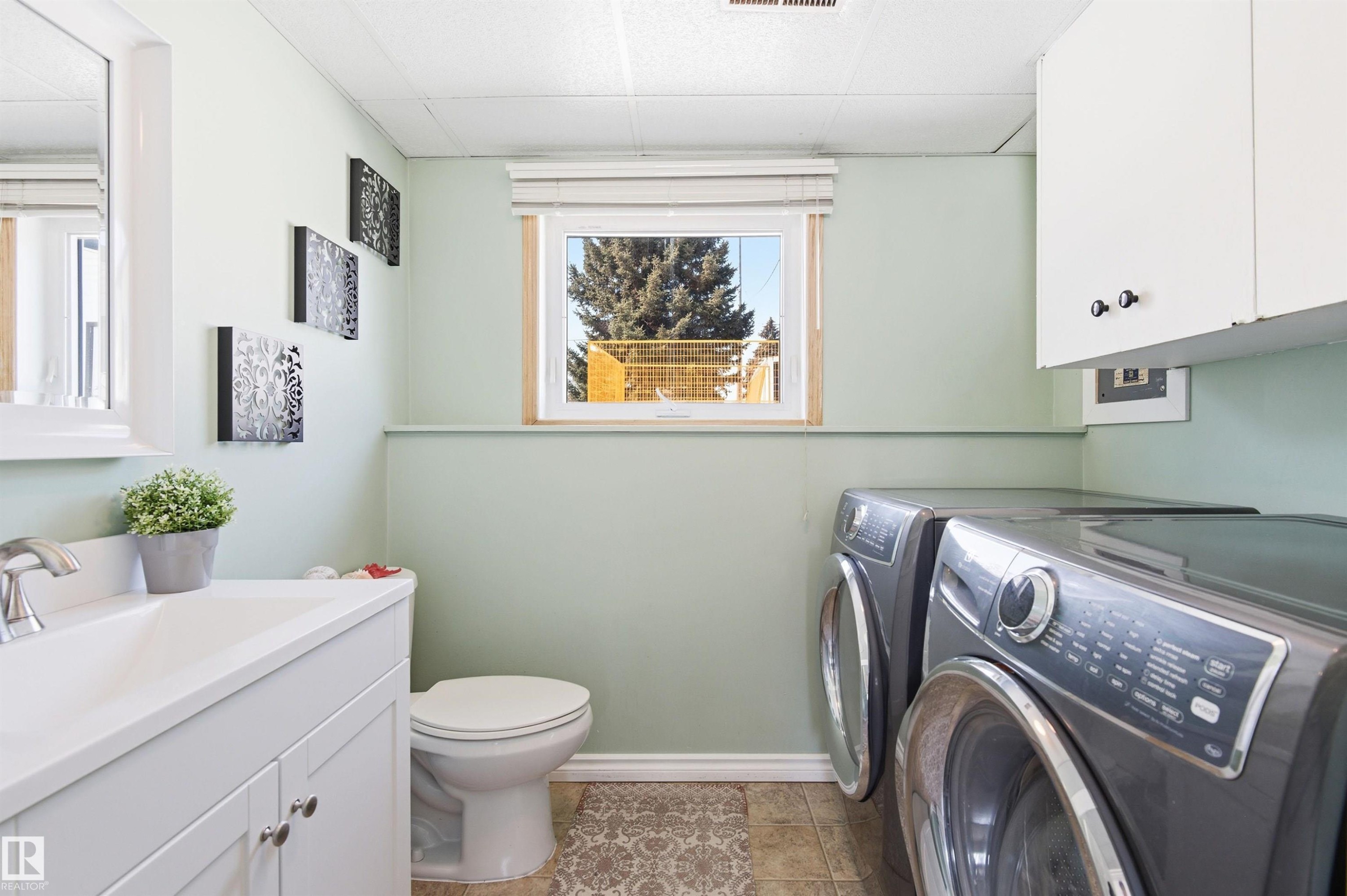 This utility space features a vanity with a sink, a toilet, a window, and laundry machines - 12904 95 Street, Edmonton, AB - Indoor Photo Showing Laundry Room