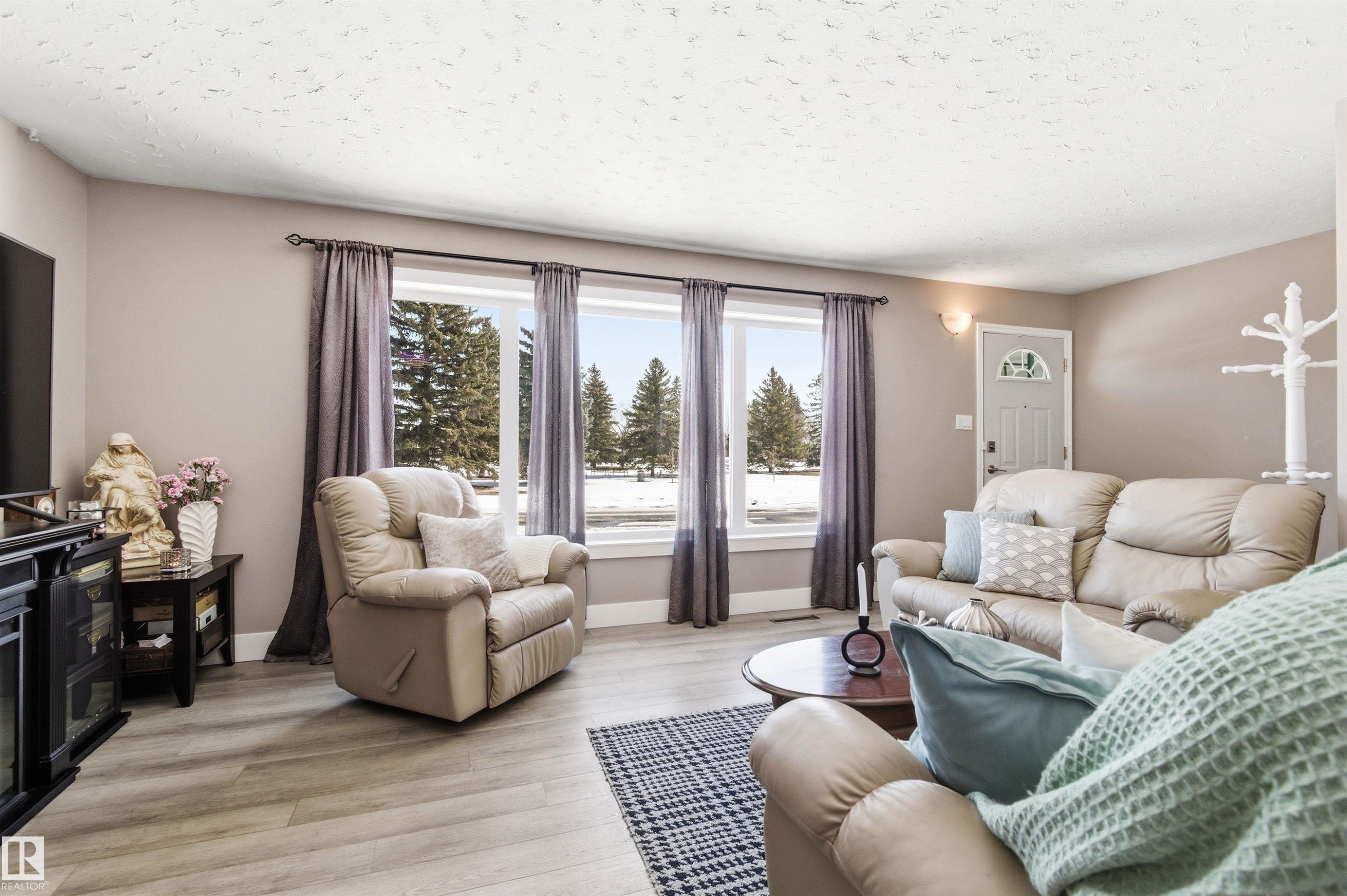 The living area features light-colored walls, light wood-style flooring, and large windows with dark curtains - 12904 95 Street, Edmonton, AB - Indoor Photo Showing Living Room