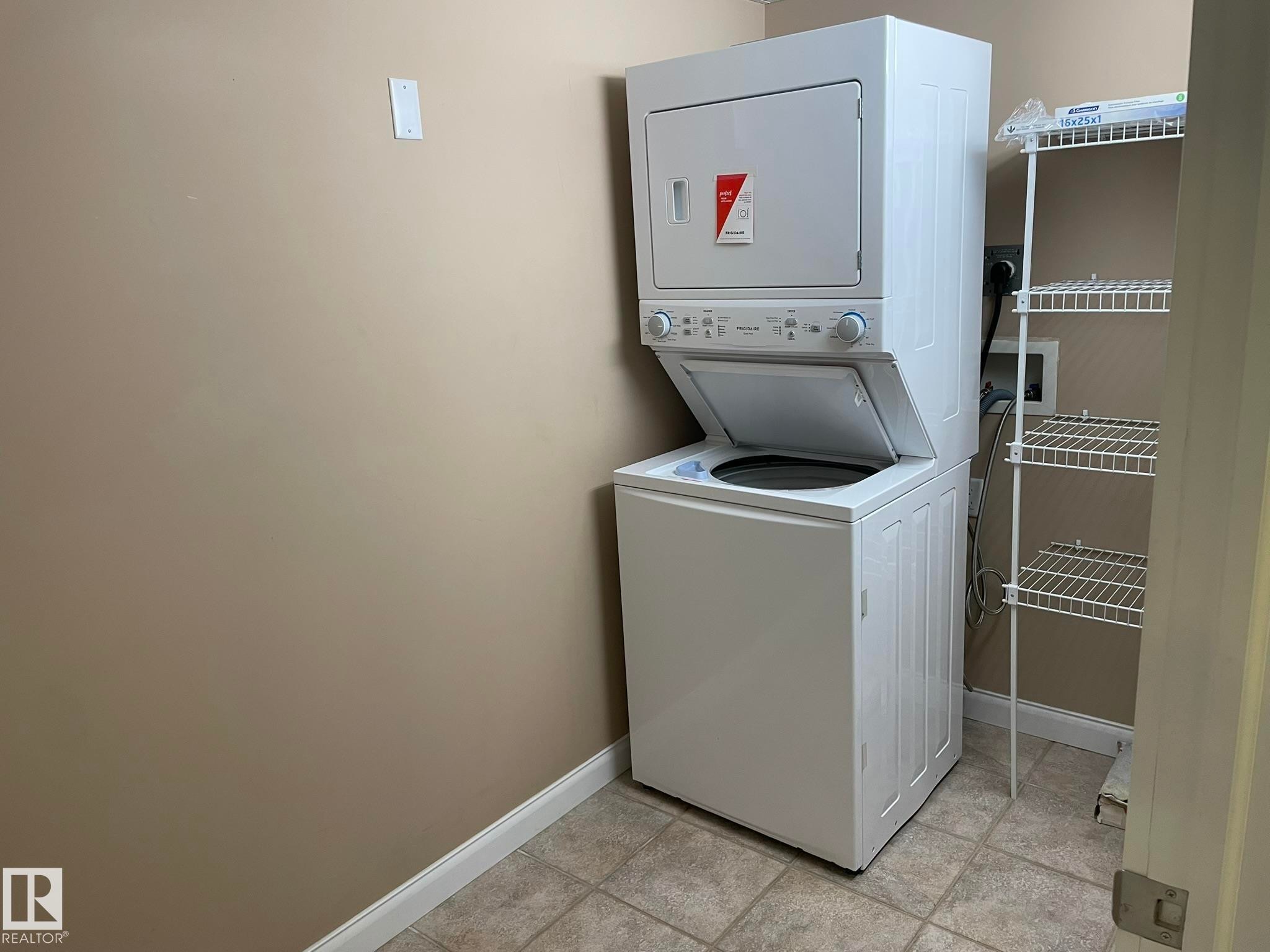 Laundry area featuring a stacked washer and dryer unit, tiled flooring, and a wire shelving unit - Edmonton, AB - Indoor Photo Showing Laundry Room