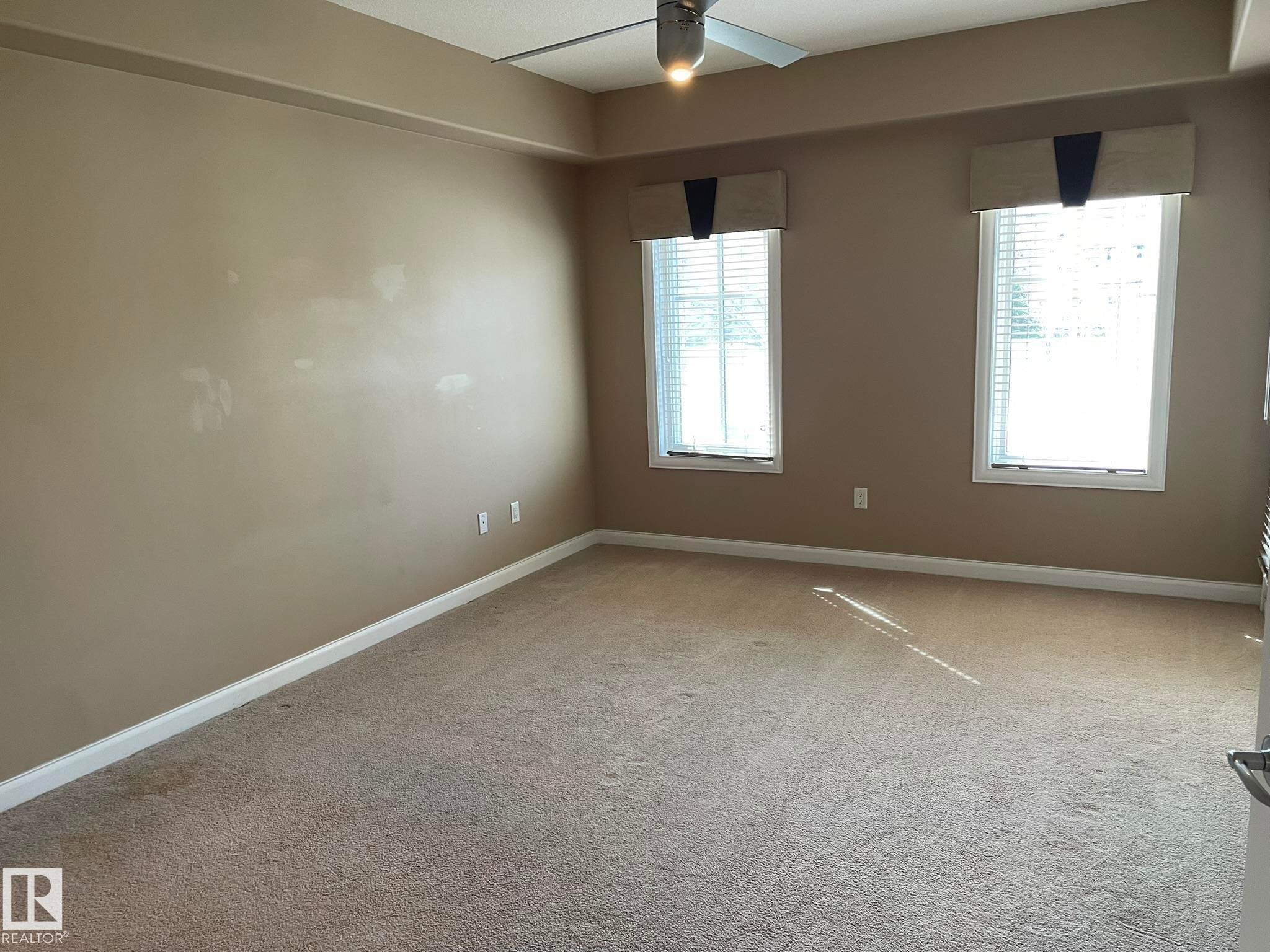 Spacious room featuring carpeted flooring, two windows with blinds, and a ceiling fan with integrated lighting - Edmonton, AB - Indoor Photo Showing Other Room
