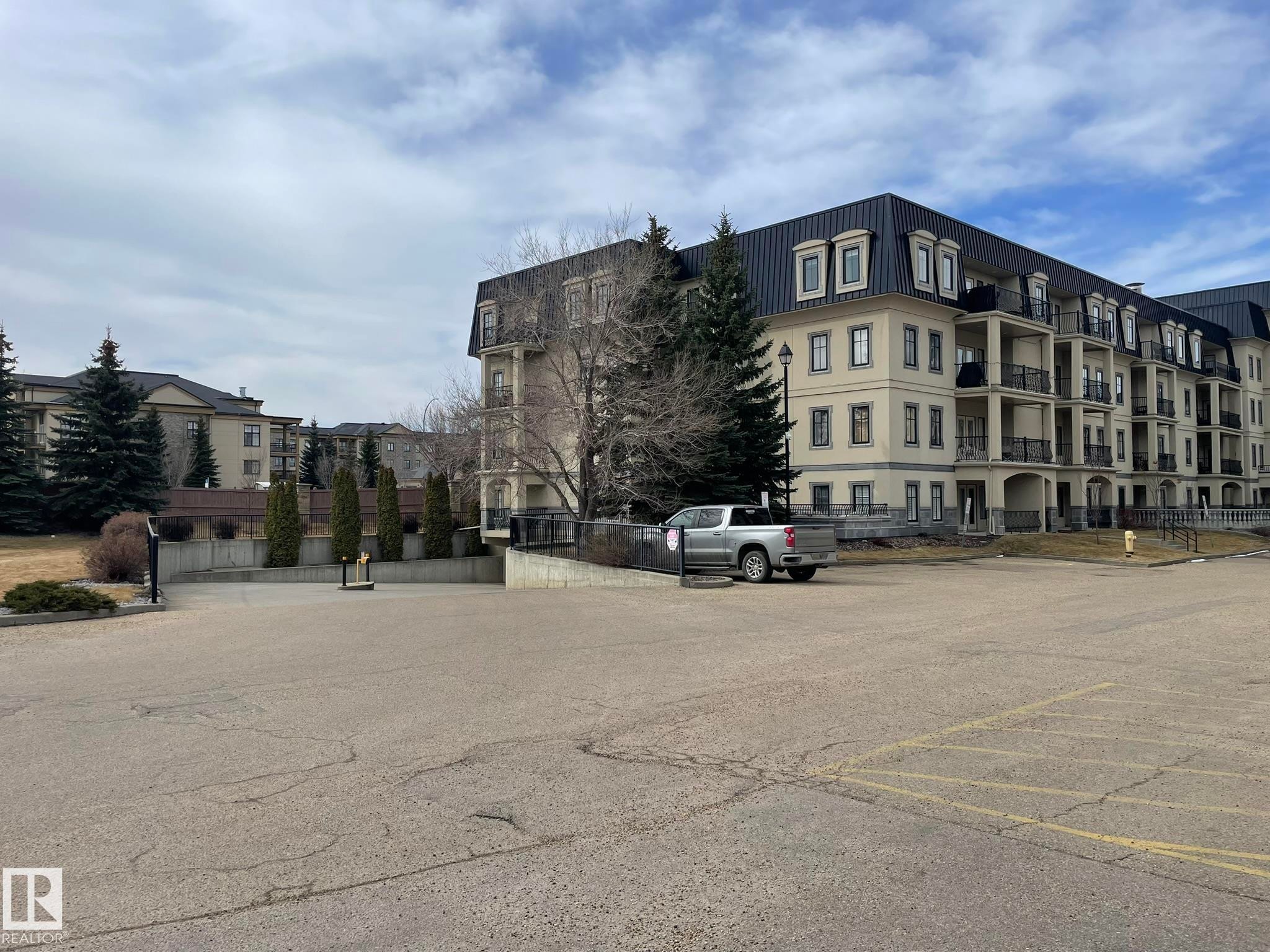 This property features a multi-story building with a distinctive dark roofline and light-colored facade - Edmonton, AB - Outdoor With Facade