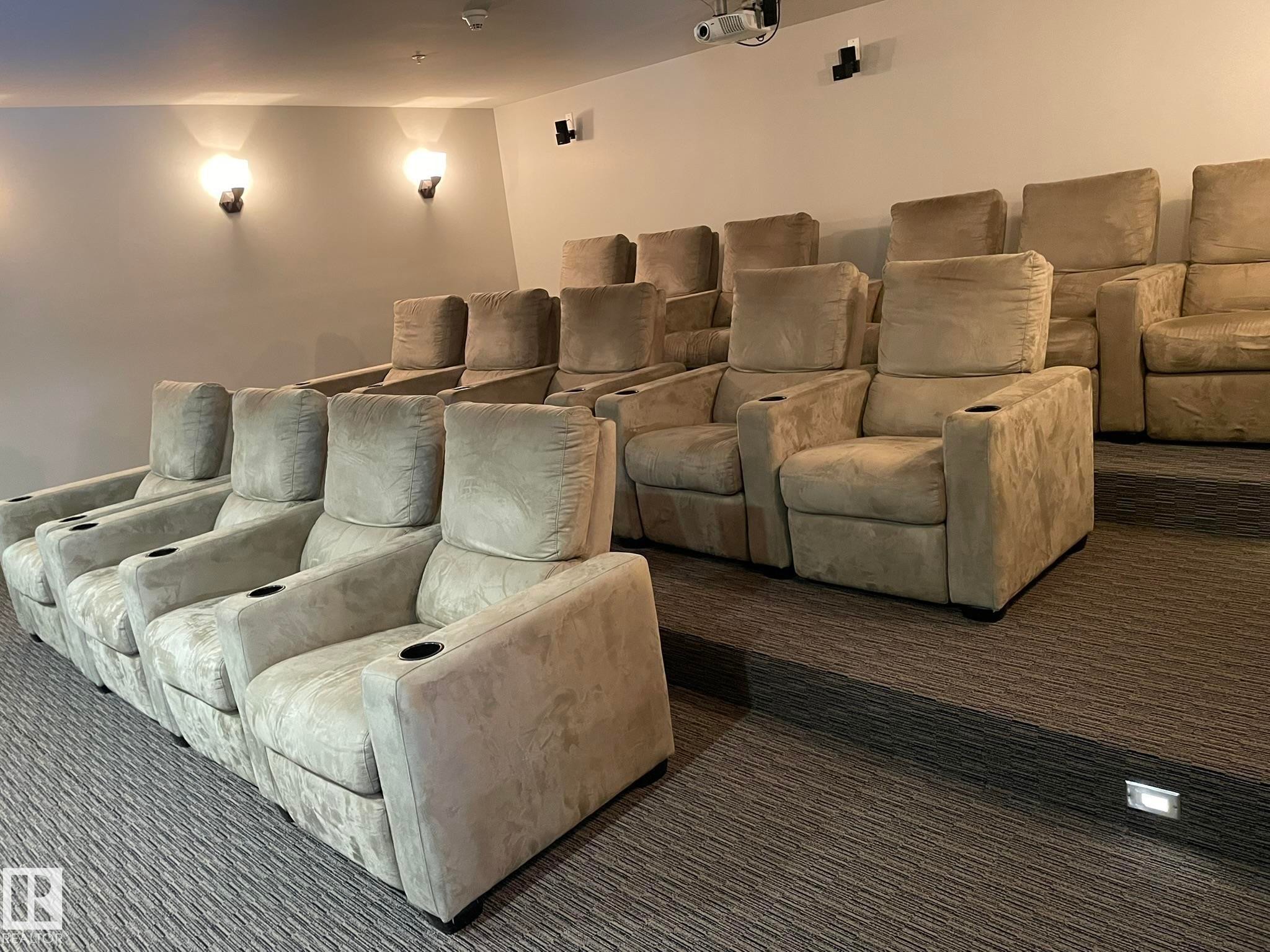 This property features a dedicated media room with tiered seating, plush upholstered recliners with integrated cup holders, and wall-mounted sconce lighting - Edmonton, AB - Indoor Photo Showing Other Room
