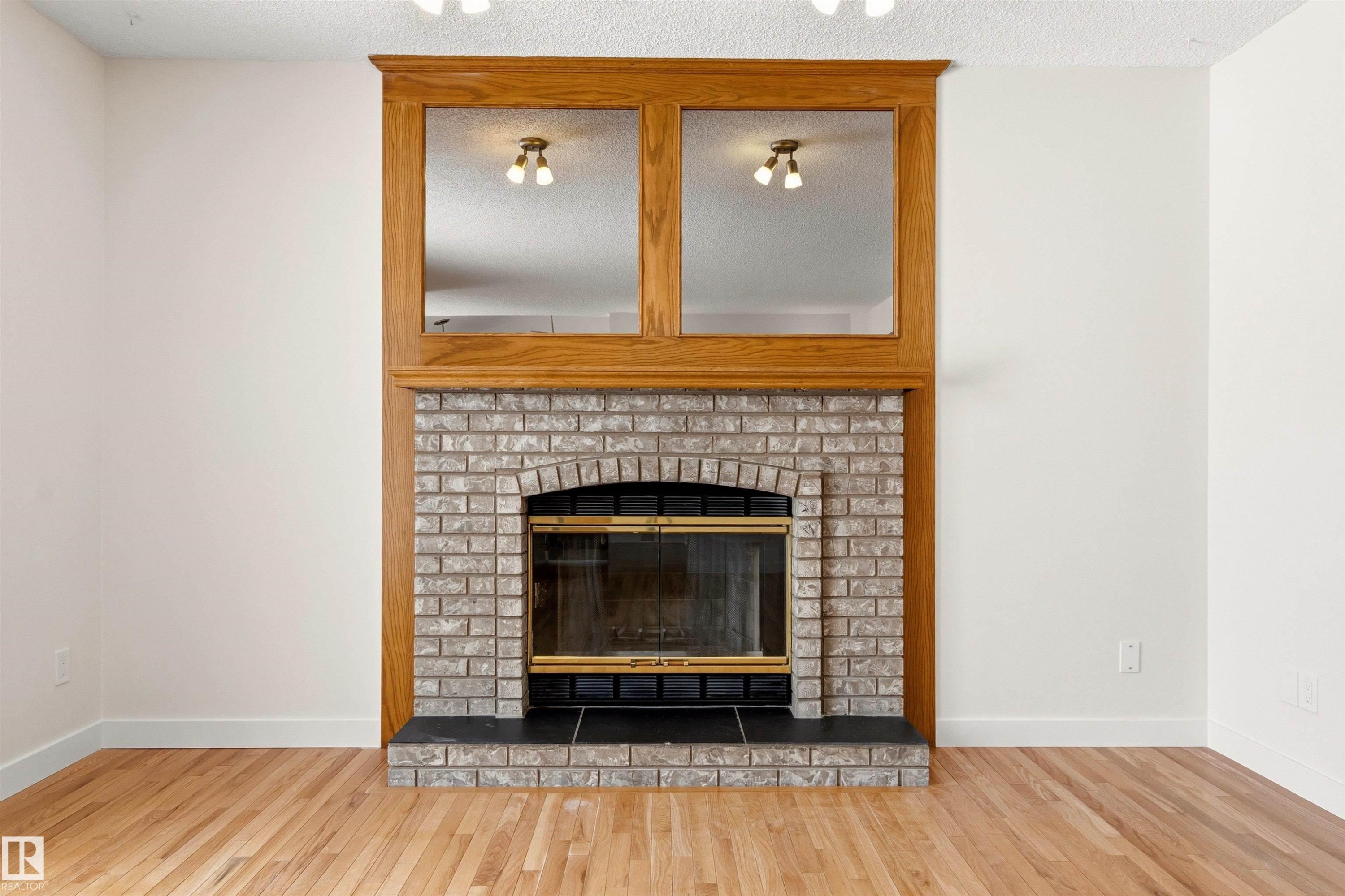 Living area featuring hardwood flooring, a fireplace with a brick surround, and a wooden mantelpiece with integrated mirrors - 3668 31A Street, Edmonton, AB - Indoor Photo Showing Living Room With Fireplace