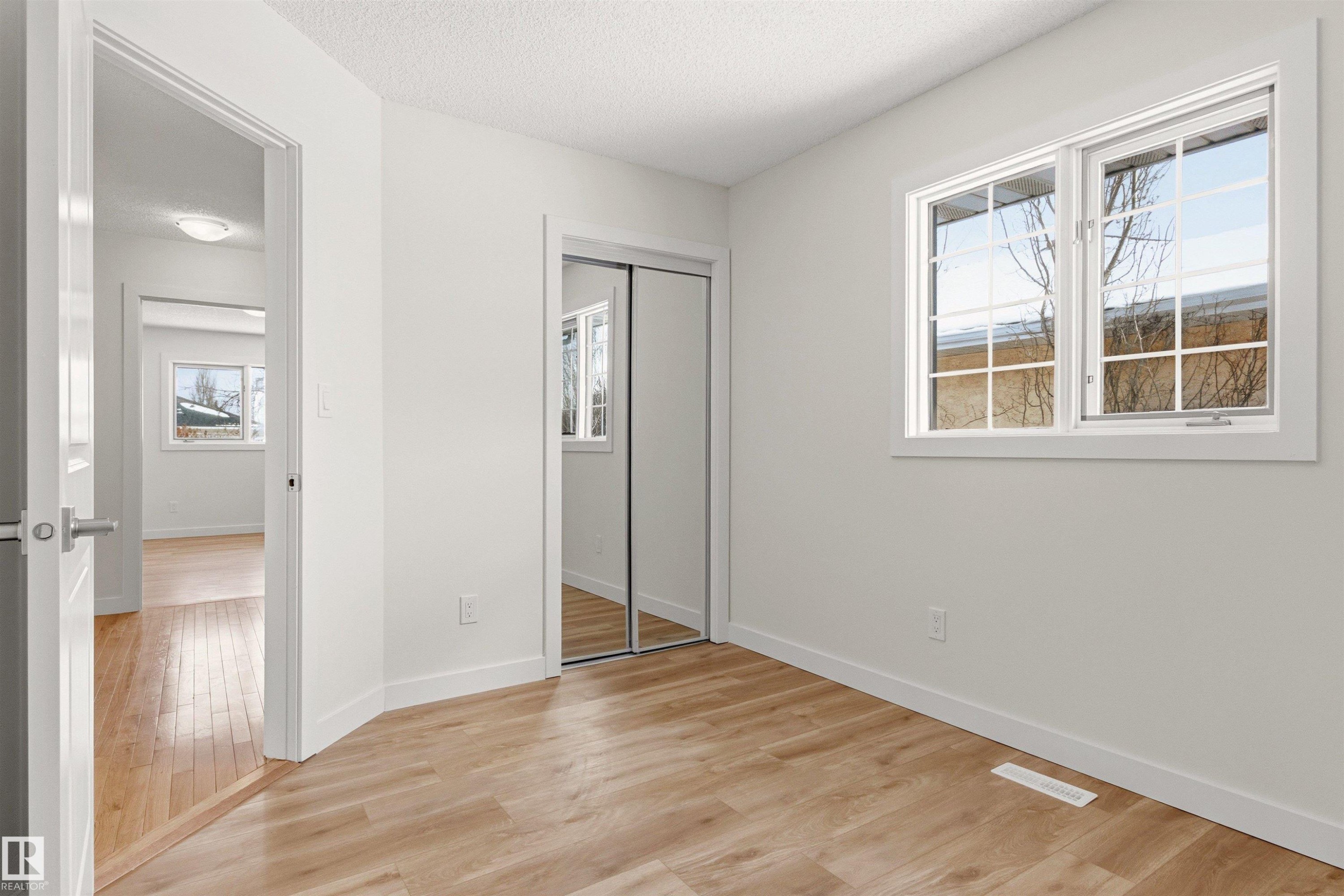 The room features light wood-style flooring, a window with white trim, and a mirrored closet - 3668 31A Street, Edmonton, AB - Indoor Photo Showing Other Room