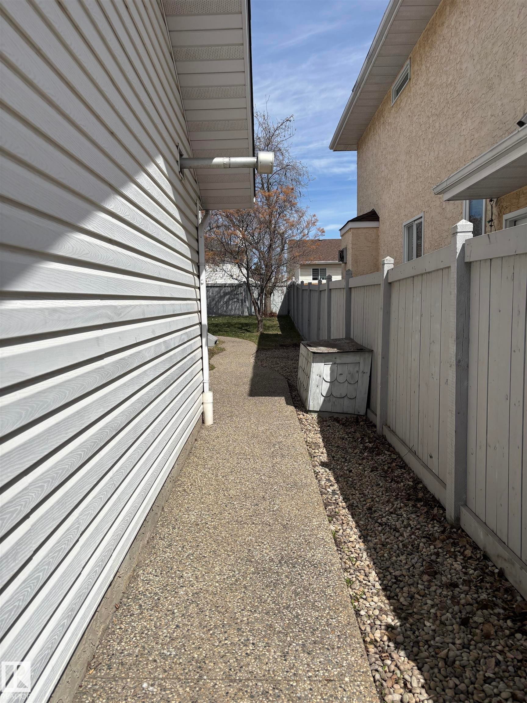 Side yard with an exposed aggregate concrete pathway and white vinyl siding - 3668 31A Street, Edmonton, AB - Outdoor With Exterior