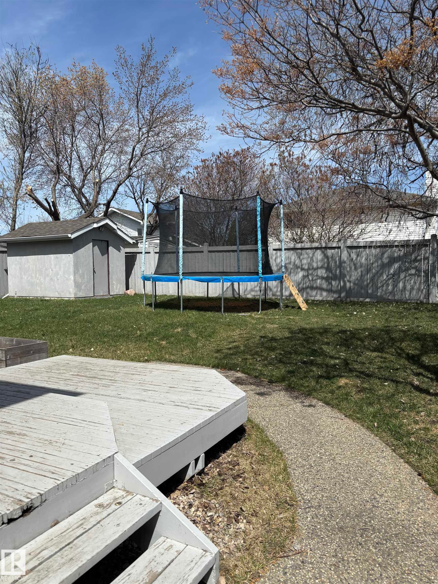 Spacious rear yard featuring an octagonal deck with steps, a concrete pathway, a storage shed, and mature trees - 3668 31A Street, Edmonton, AB - Outdoor
