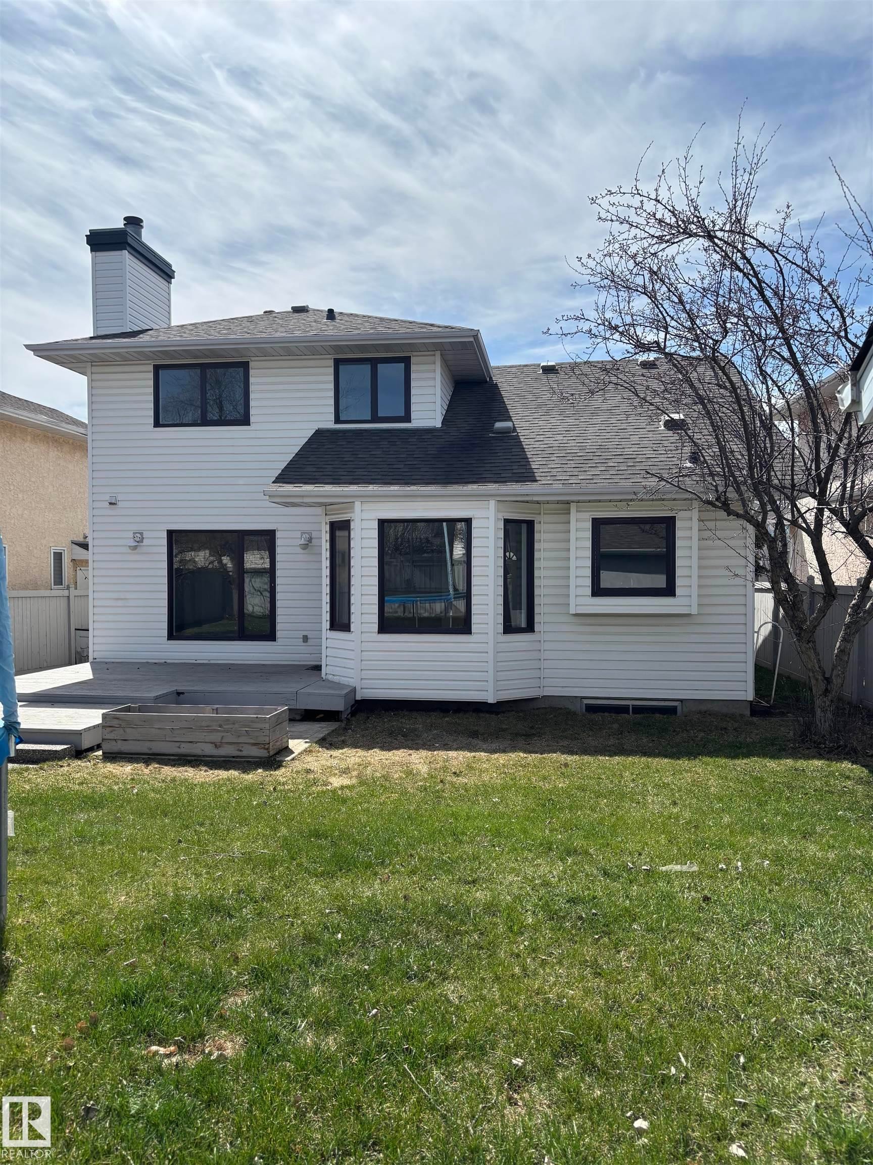 Rear exterior featuring white horizontal siding, dark-framed windows, a multi-level deck, and a raised planter box - 3668 31A Street, Edmonton, AB - Outdoor