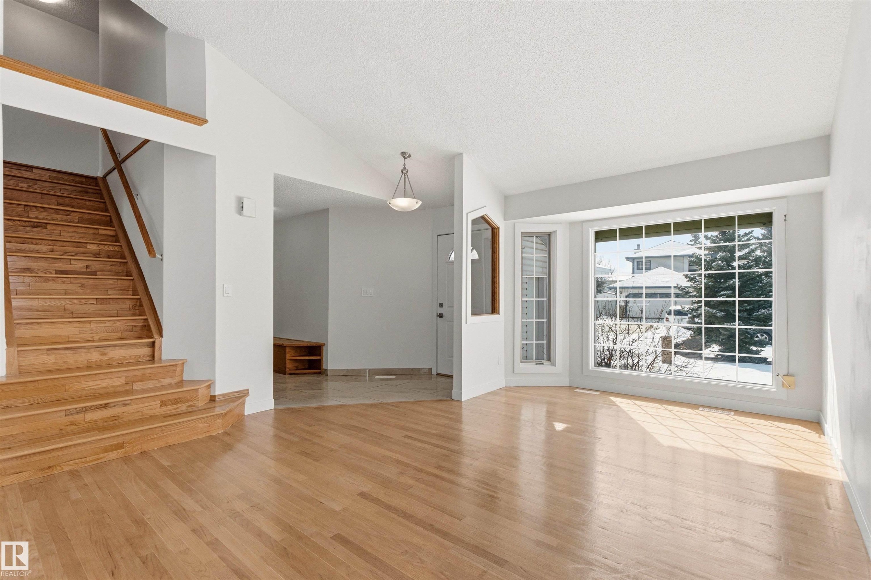 This bright living space features hardwood floors, a large bay window, and a grand wooden staircase - 3668 31A Street, Edmonton, AB - Indoor Photo Showing Other Room