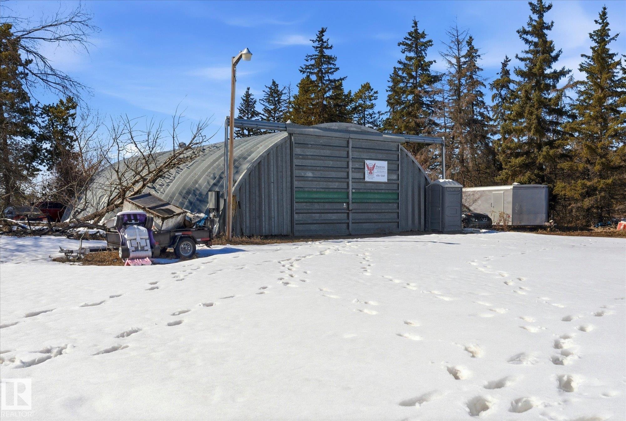 Quonset building with a metal exterior, overhead lighting fixture, and surrounding evergreen trees - 25750 18 Street, Edmonton, AB - Outdoor