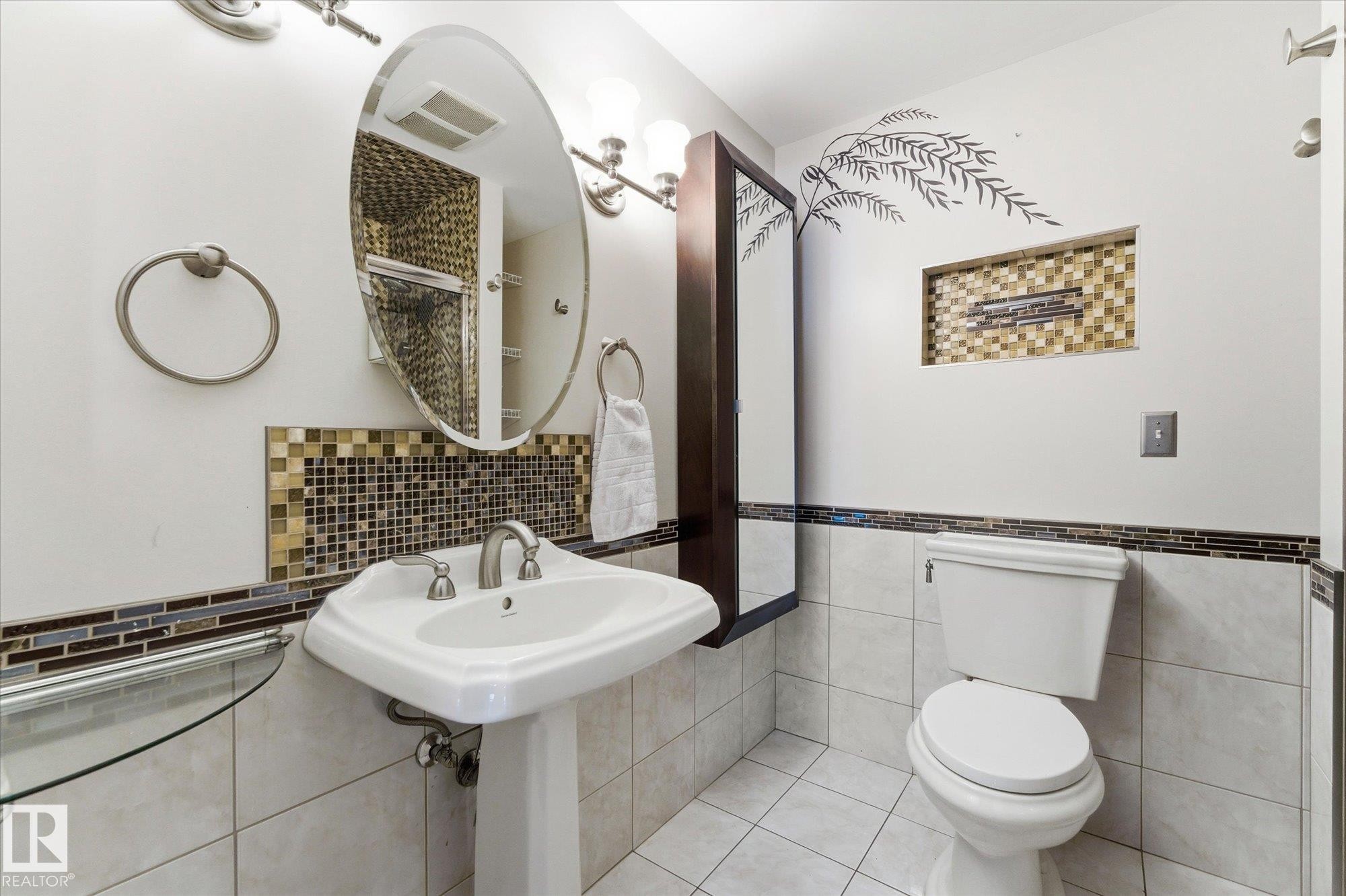 Bathroom featuring a white pedestal sink with brushed nickel faucet, an oval mirror, and an adjacent toilet - 25750 18 Street, Edmonton, AB - Indoor Photo Showing Bathroom