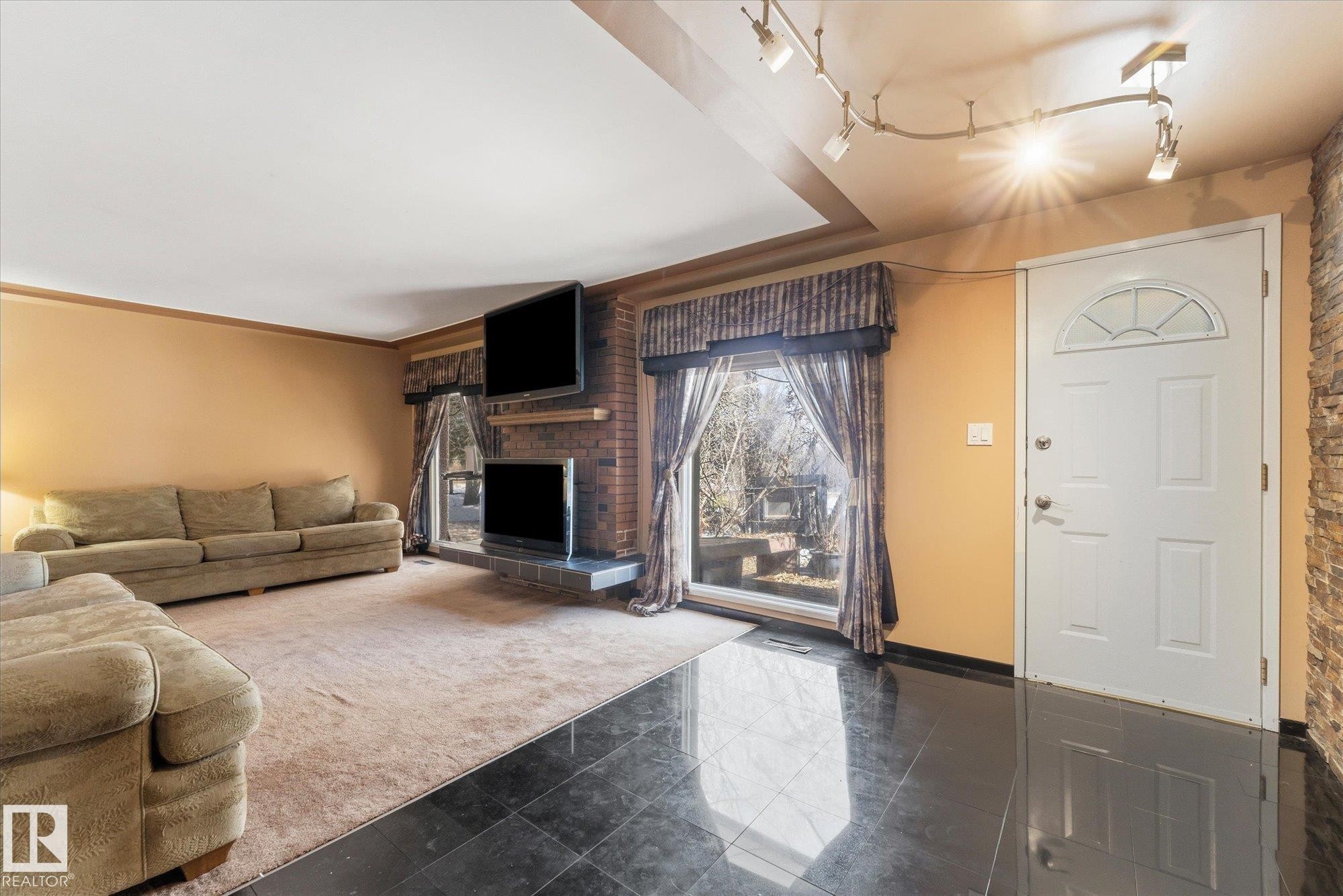 Living area featuring black tile flooring, a white paneled entry door with a decorative fanlight, and a brick fireplace - 25750 18 Street, Edmonton, AB - Indoor Photo Showing Living Room With Fireplace