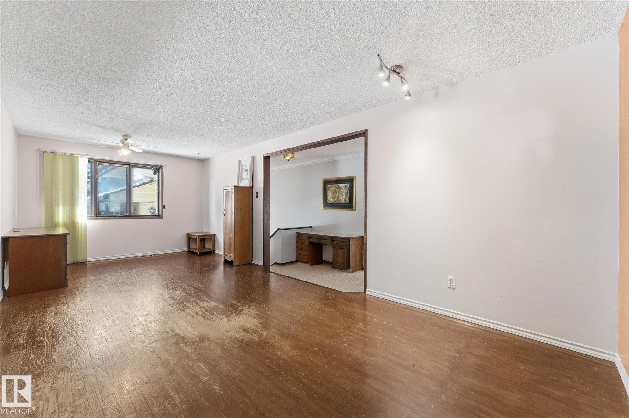 Spacious interior room with wood-finish flooring, a ceiling fan, and a large window providing natural illumination - 25750 18 Street, Edmonton, AB - Indoor