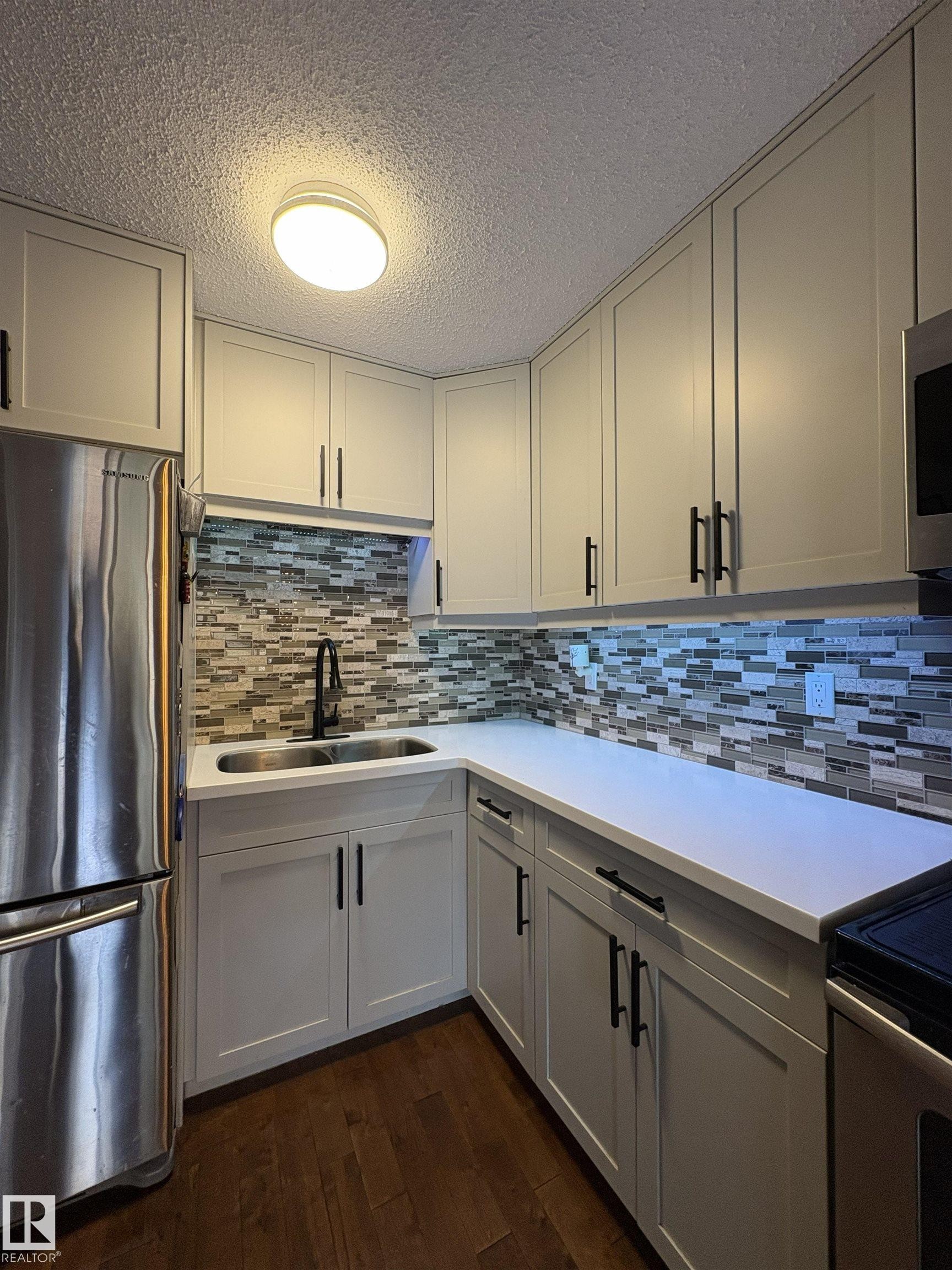 Modern kitchen featuring light-toned cabinetry with matte black hardware, white countertops, and a tiled backsplash - 79 Akinsdale Gardens, St. Albert, AB - Indoor Photo Showing Kitchen With Double Sink With Upgraded Kitchen