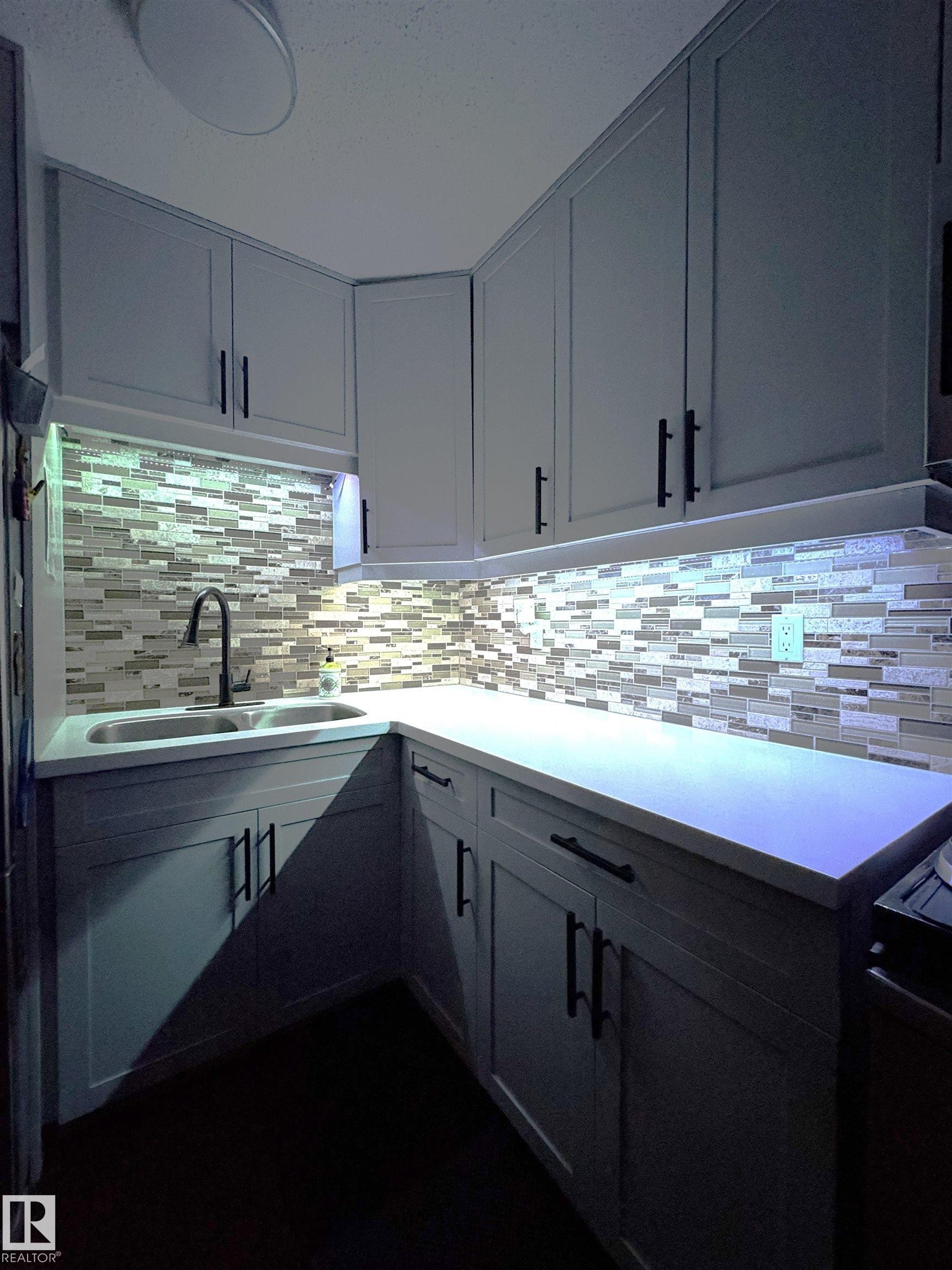L-shaped kitchen with light-toned cabinetry and matte black hardware, featuring a double basin stainless steel sink and a mosaic tile backsplash - 79 Akinsdale Gardens, St. Albert, AB - Indoor Photo Showing Kitchen With Upgraded Kitchen