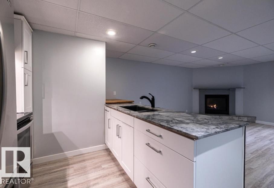 The kitchen features a center island with a dark sink, a black faucet, and a patterned countertop, with light wood-style flooring throughout - 71 Labelle Crescent, St. Albert, AB - Indoor Photo Showing Other Room