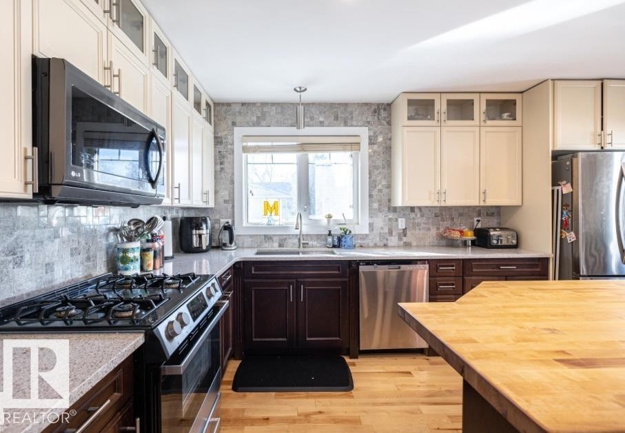 The kitchen features a gas range with an overhead microwave, stainless steel appliances, and a mosaic tile backsplash - 71 Labelle Crescent, St. Albert, AB - Indoor Photo Showing Kitchen With Upgraded Kitchen