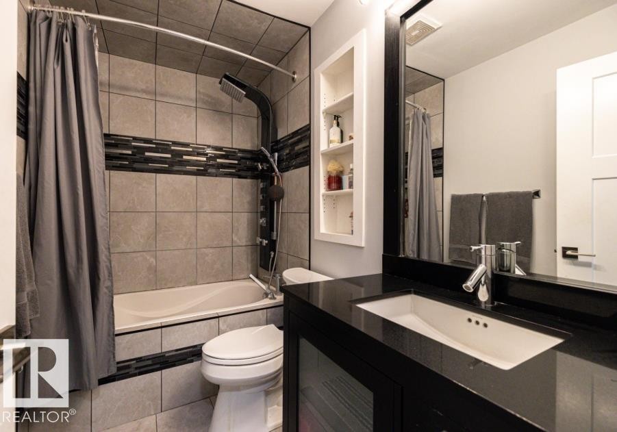This bathroom features a shower/tub combination with tiled walls, a black vanity with an integrated sink, and a large mirror - 71 Labelle Crescent, St. Albert, AB - Indoor Photo Showing Bathroom
