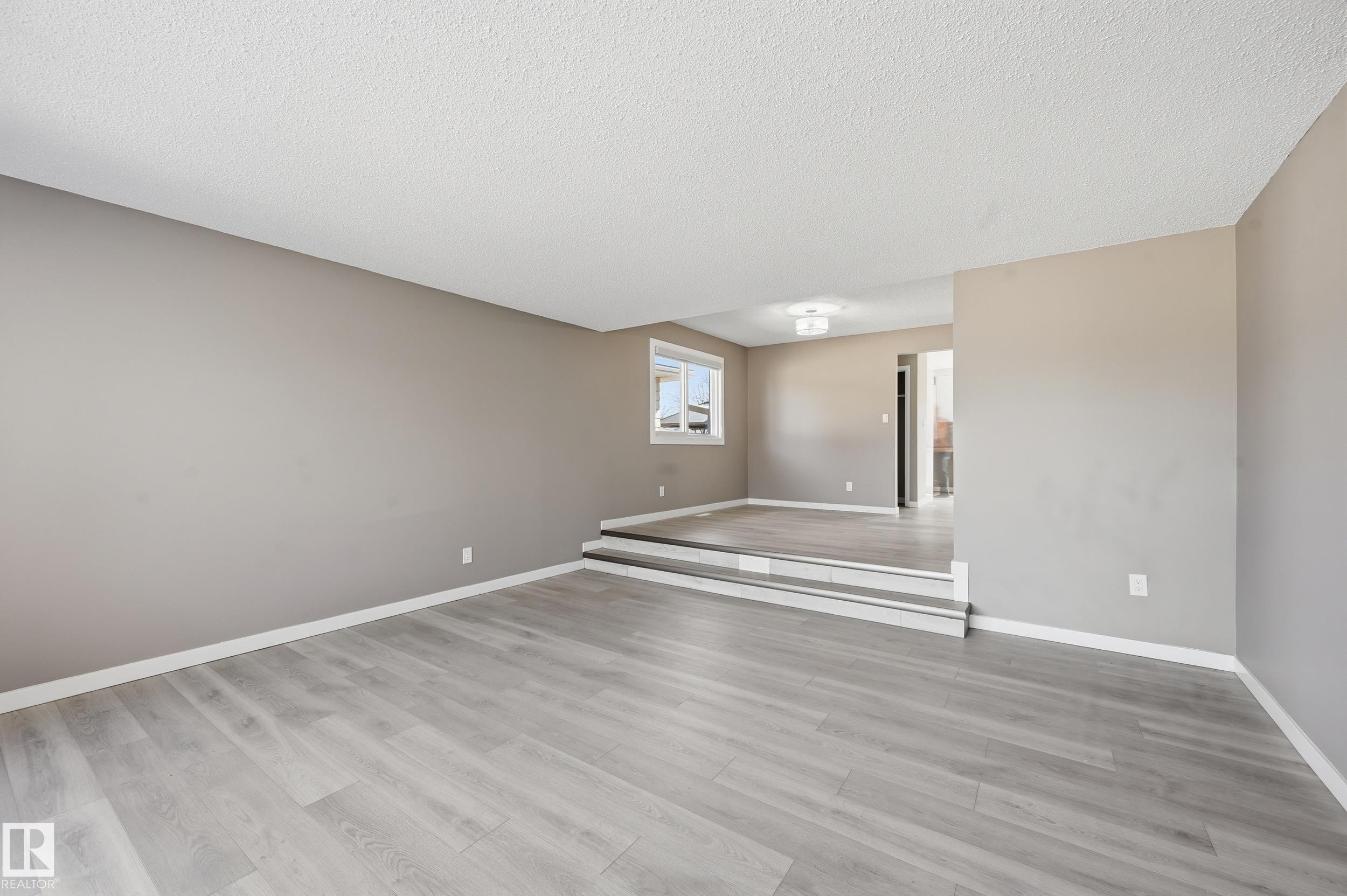 The expansive living area features light-toned flooring, neutral wall paint, and a multi-level design - 6907 19 Avenue, Edmonton, AB - Indoor Photo Showing Other Room