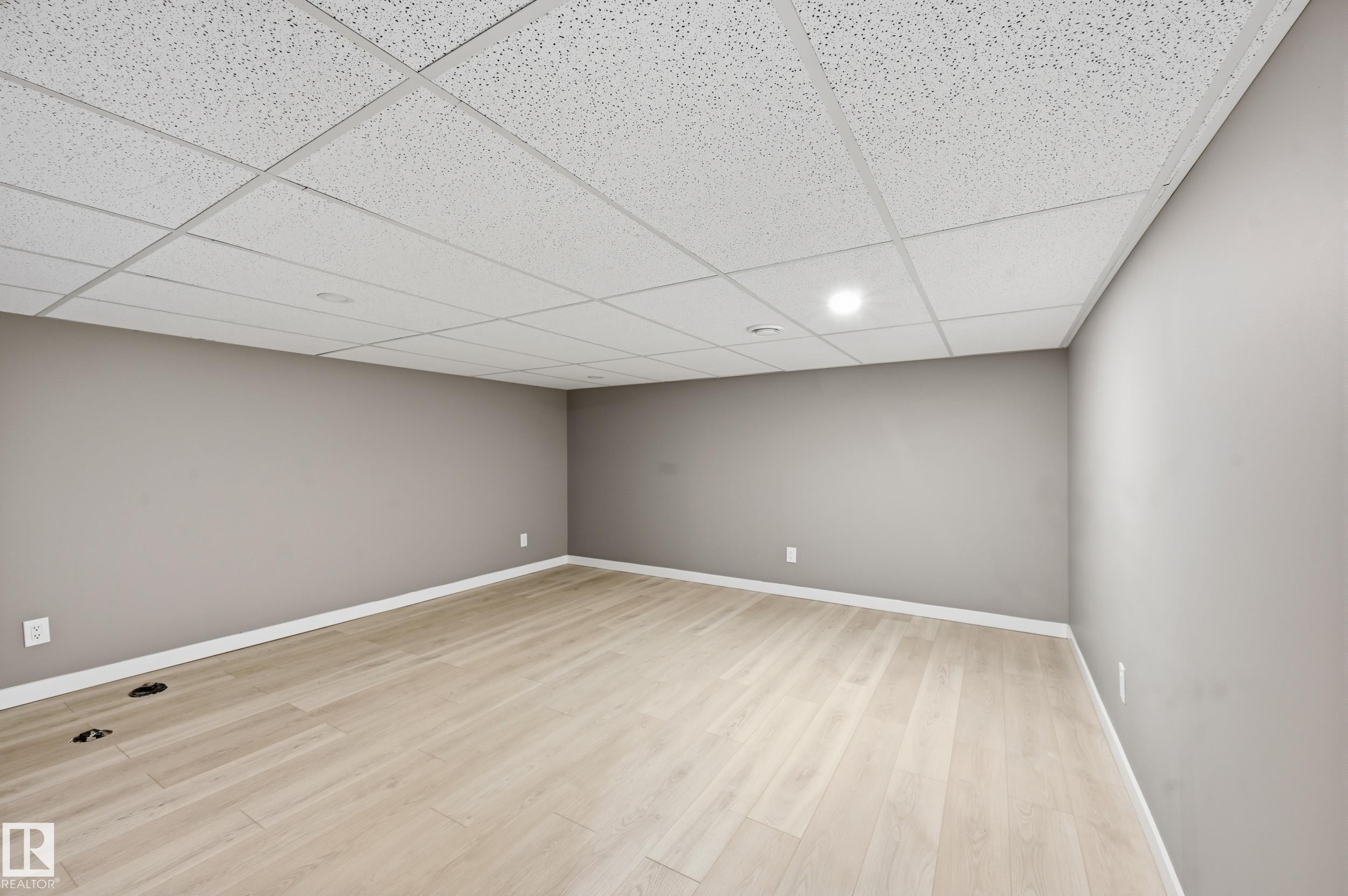 Expansive room featuring light-colored flooring, neutral-toned walls, and a white grid ceiling with recessed lighting - 6907 19 Avenue, Edmonton, AB - Indoor